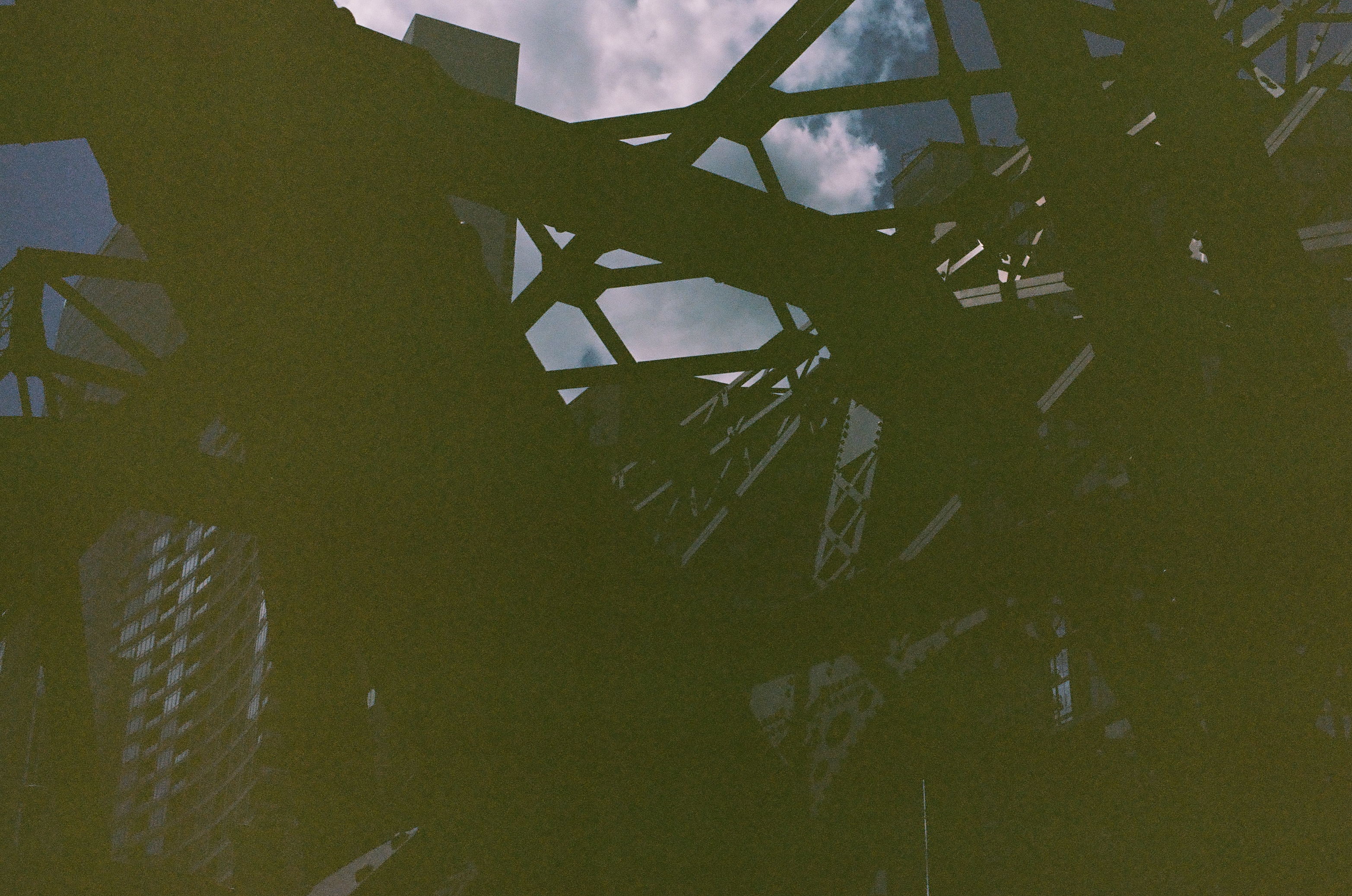 Shadowed figures gather beneath a dense steel structure while bright clouds break through the open framework.