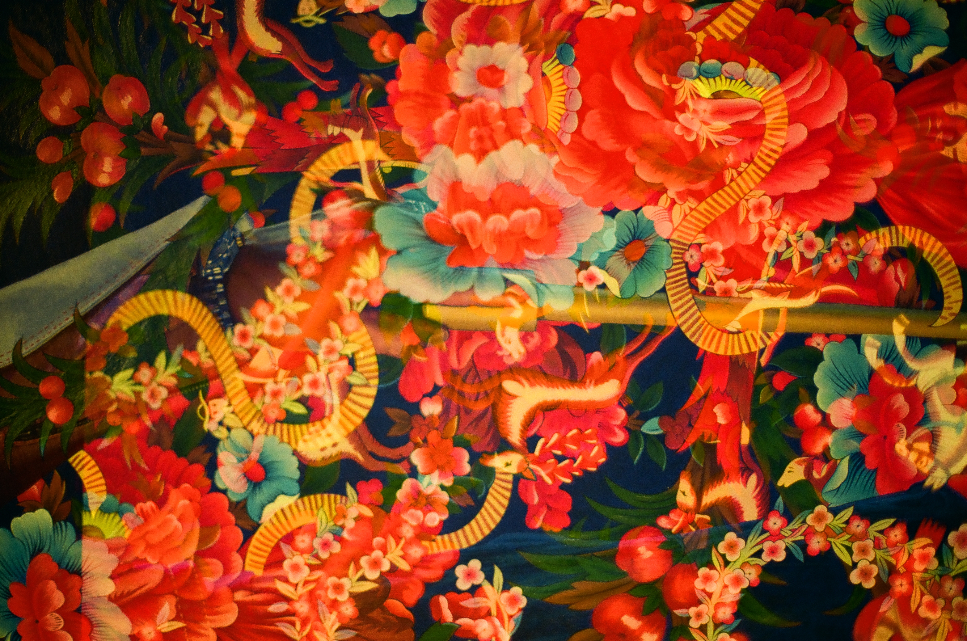 Dense red and orange flowers surround green leaves and two long reflective forms on a dark patterned surface.