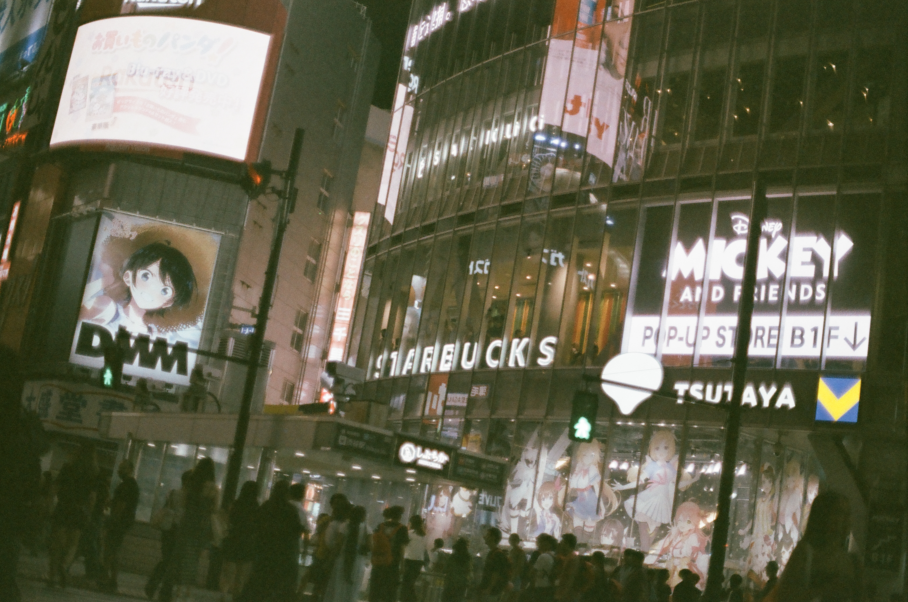 A curved glass building lettered 'STARBUCKS' rises beside a sign reading 'MICKEY AND FRIENDS POP-UP STORE B1F' above a lit crosswalk.