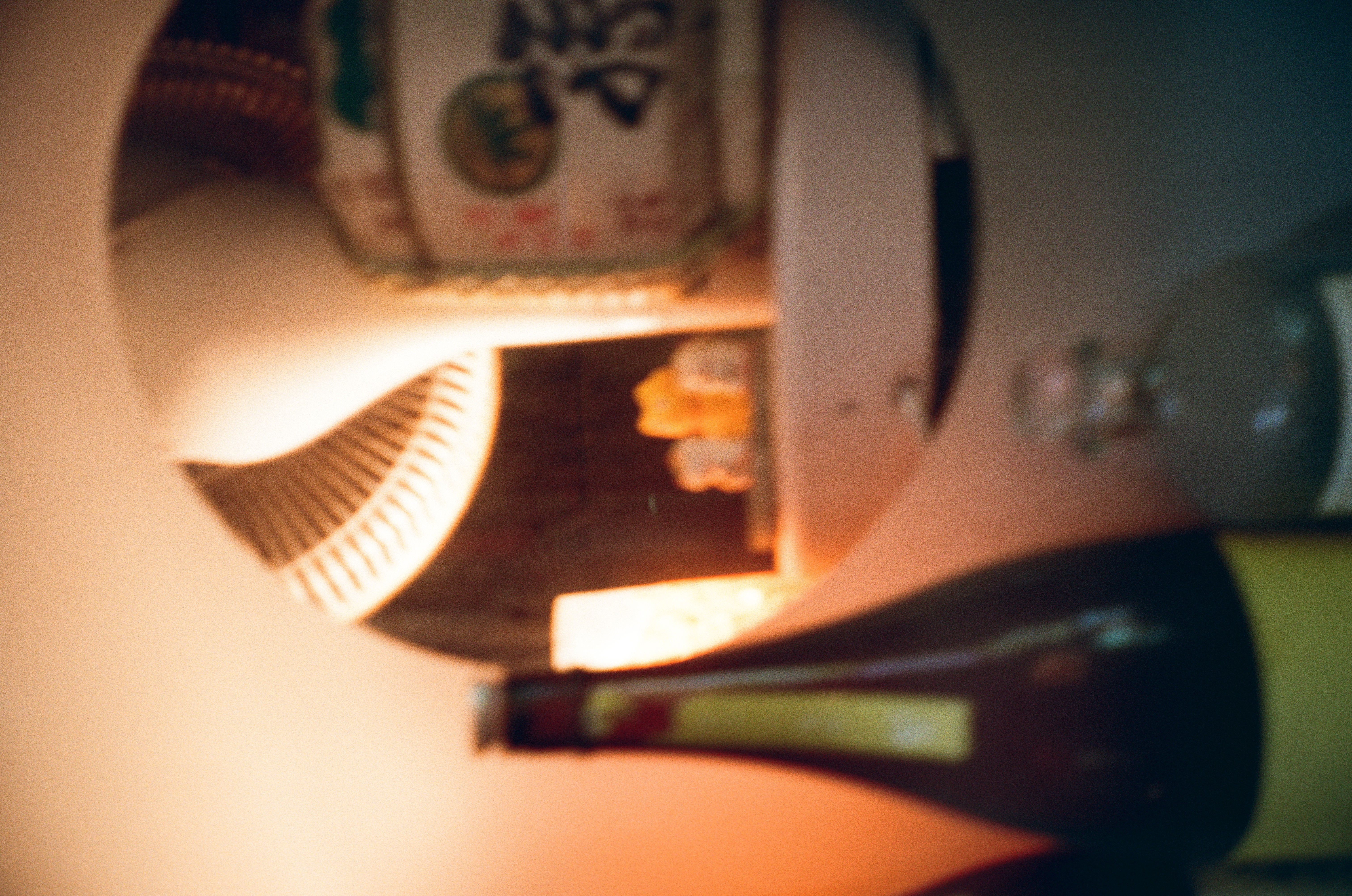 A dark bottle stands out of focus before a round mirror reflecting a fan-shaped lamp, beside a barrel marked with brushed calligraphy.