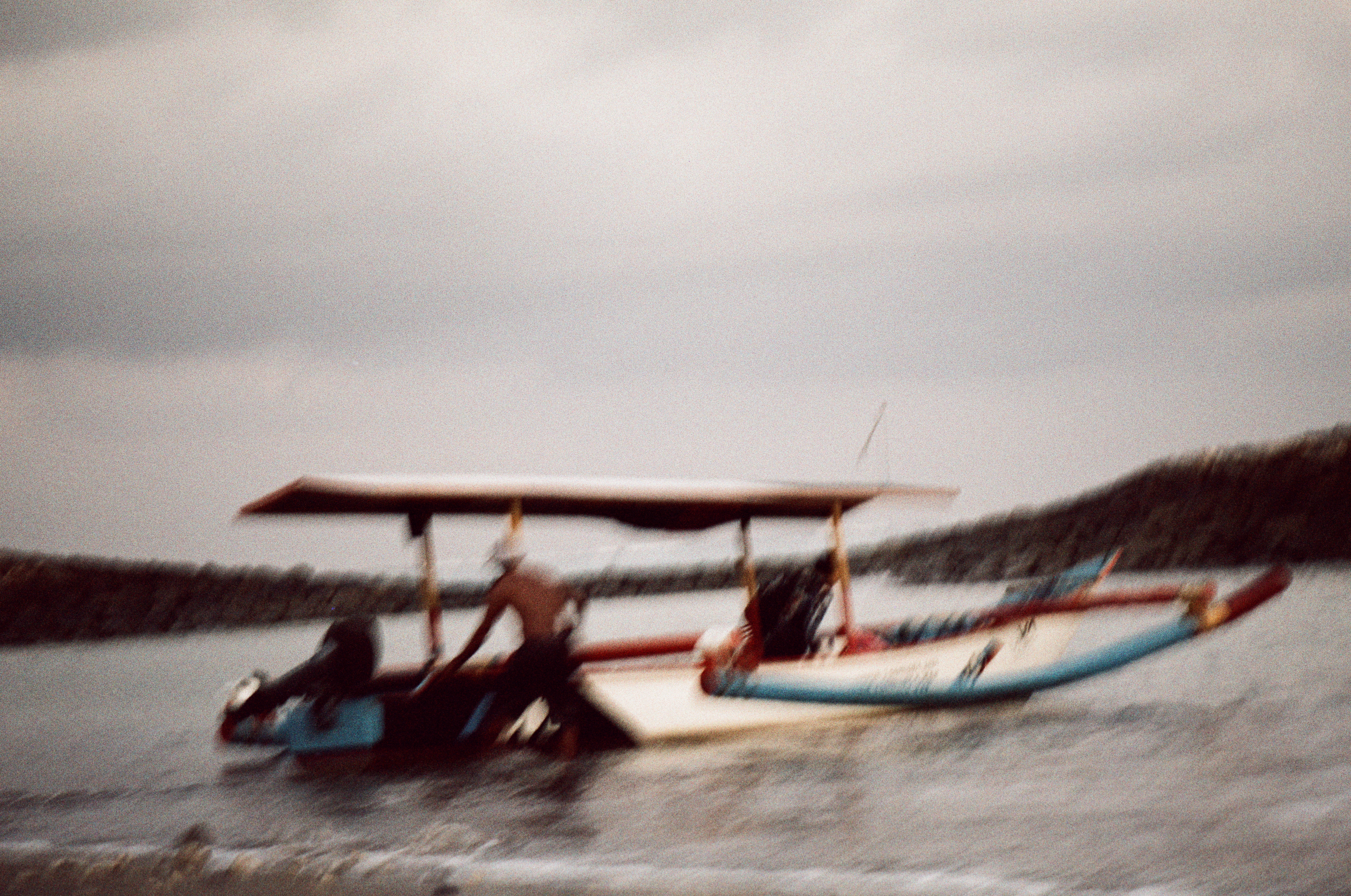 Two boats sit in churned shallow water, one under a flat canopy, as a man bends at the stern below an overcast sky.