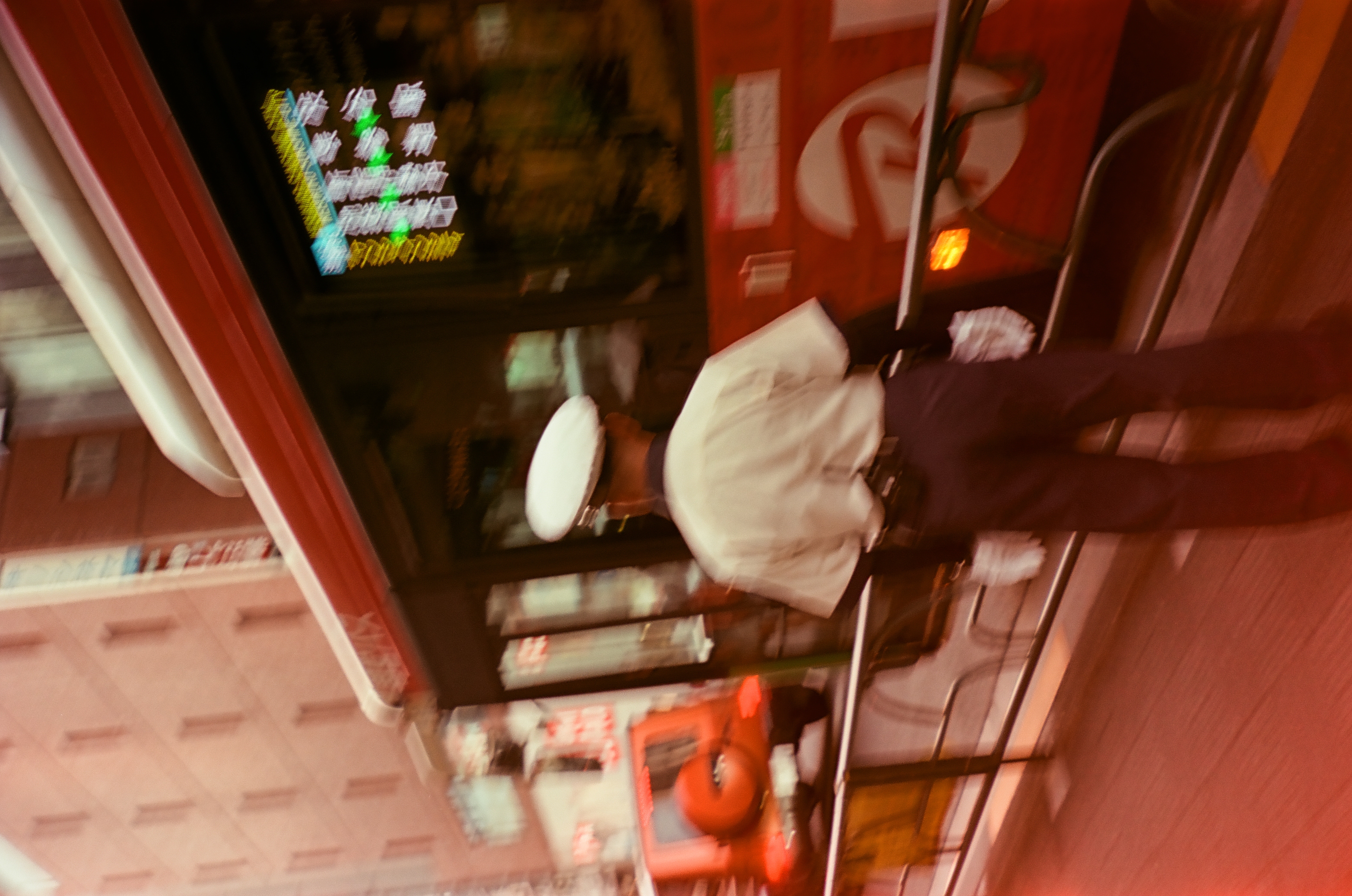 A uniformed person in a white cap and white gloves stands at a metal guardrail as a red bus passes with a blurred lit display.