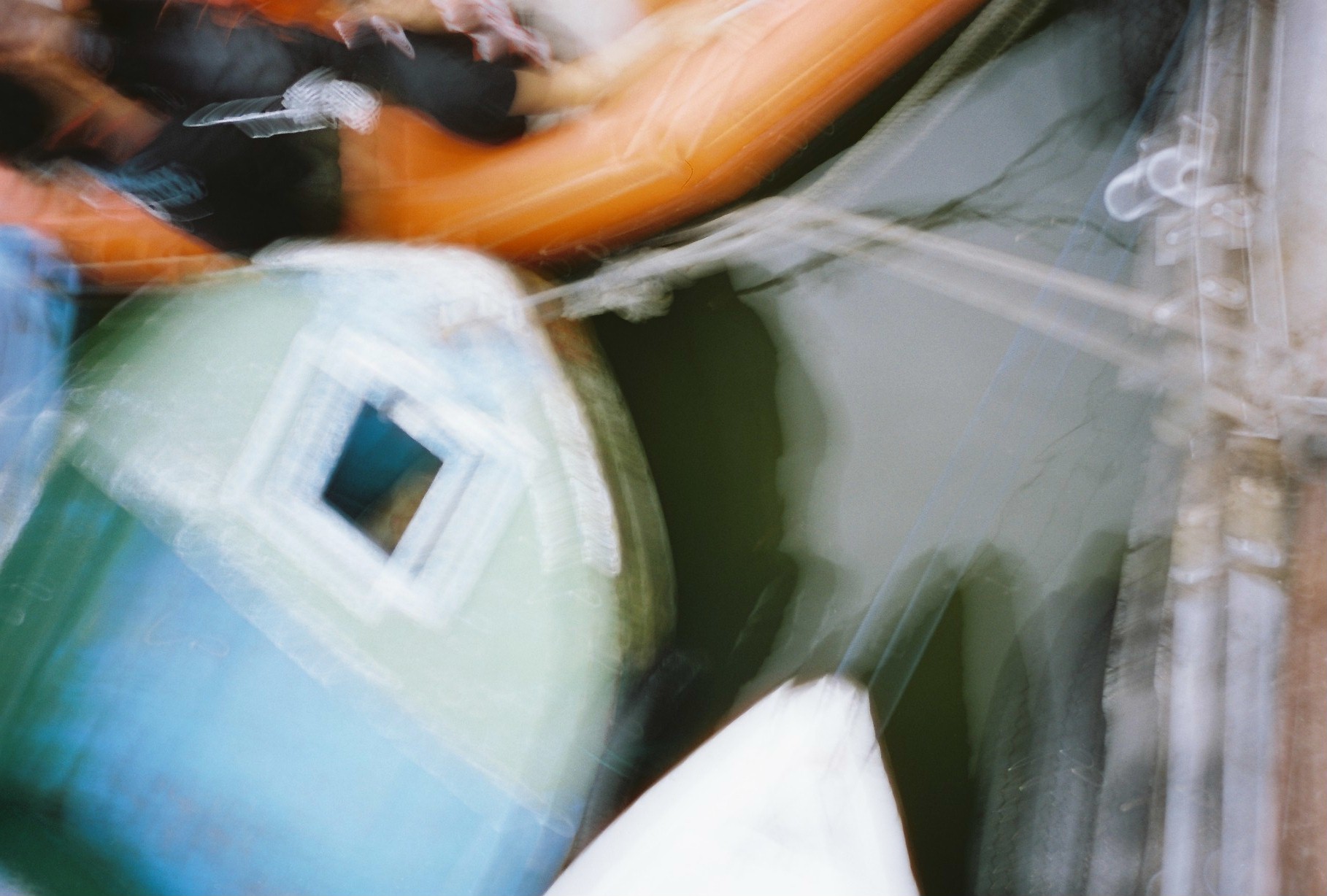 Overlapping orange, blue, green, black, and white shapes sweep diagonally across the frame with pronounced blur and repeated edges.