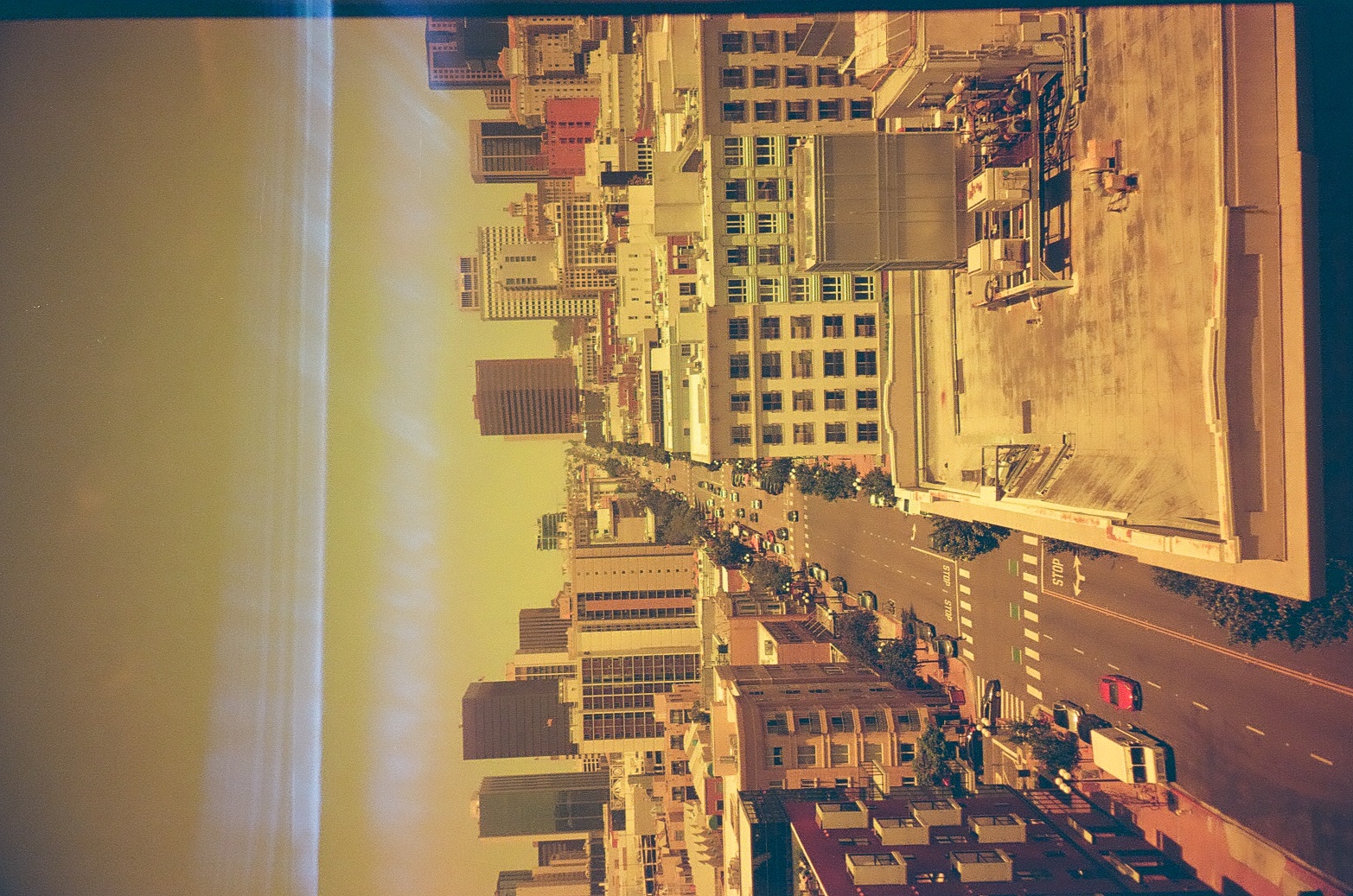 An elevated view looks down a downtown street grid crowded with buildings and moving cars, painted STOP lettering visible on the pavement below, all cast in warm amber haze.