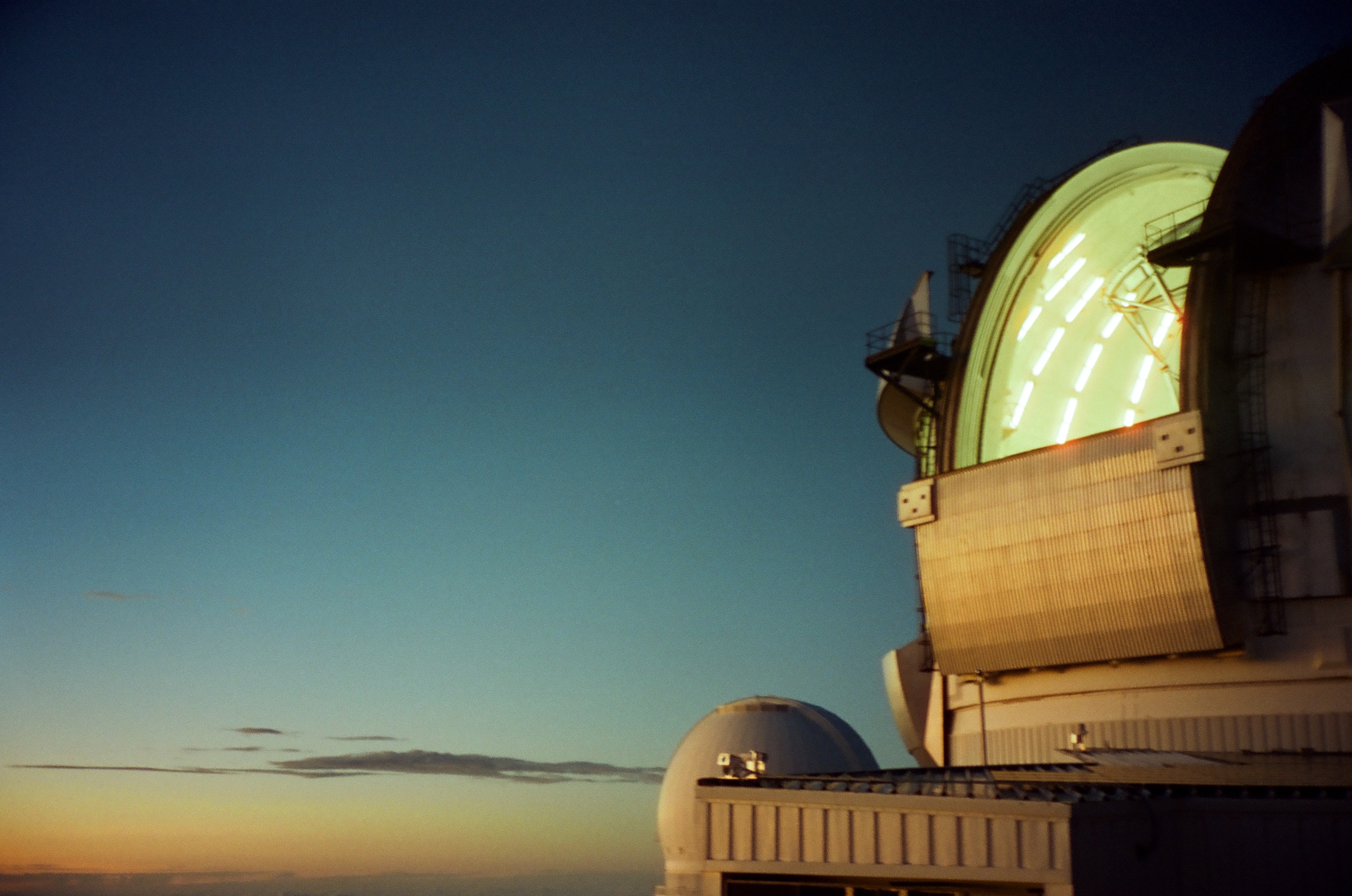 A large pale observatory dome opens to reveal green interior light above a smaller rounded structure.