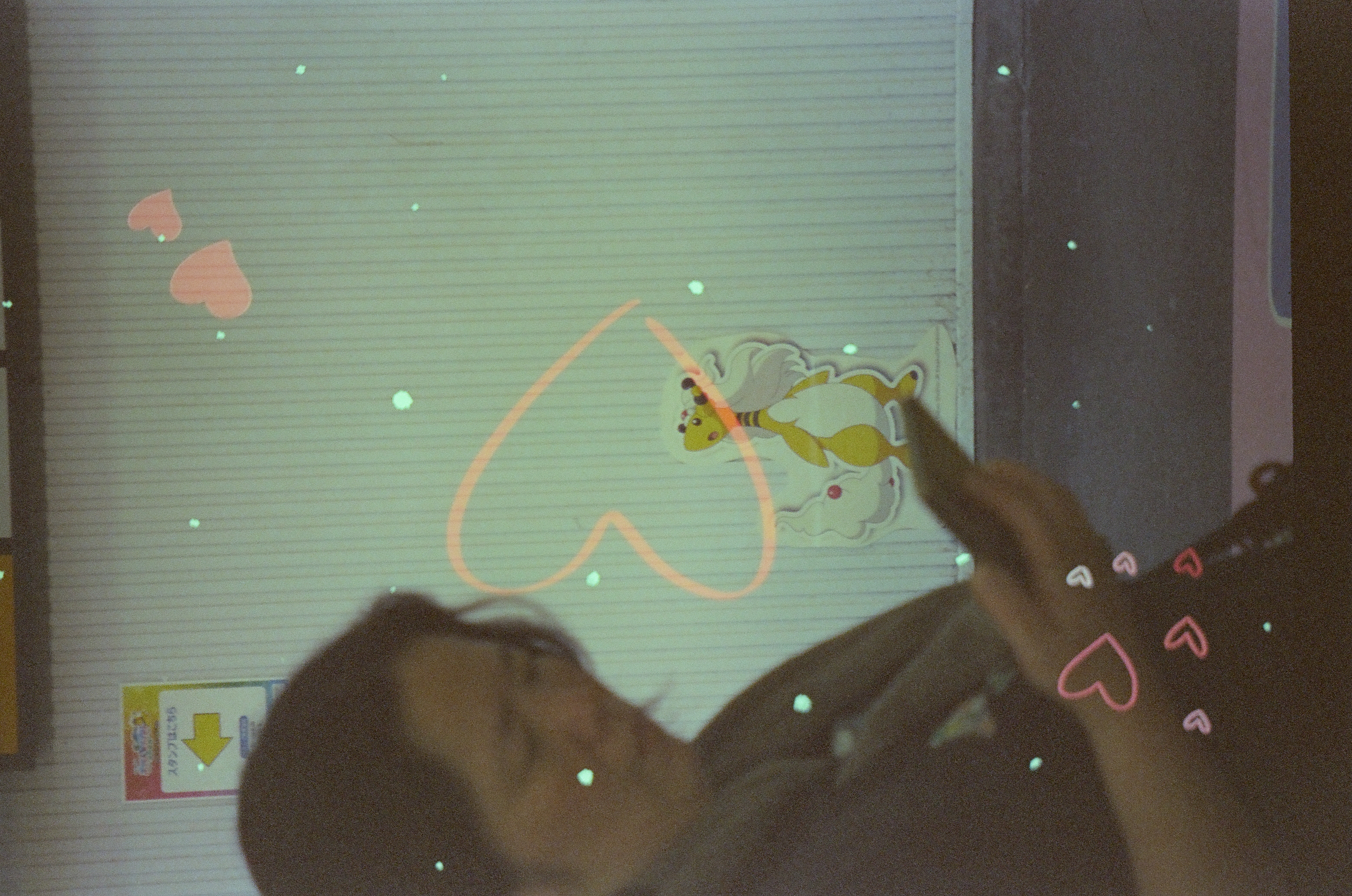 A person looks at a phone in front of a wall sticker of a cartoon animal character, circled by a hand-drawn orange heart outline and additional heart shapes.