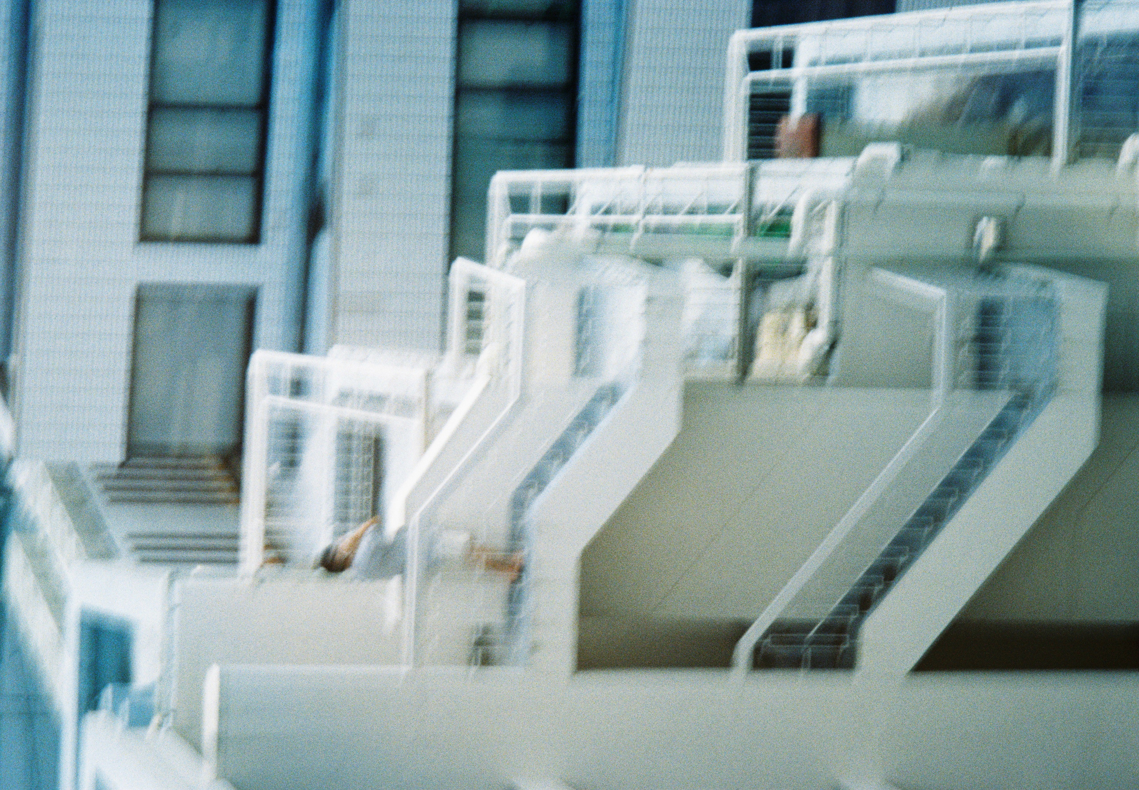 A motion-blurred white apartment block shows zigzagging exterior stairways and balcony rails, with one figure leaning on an upper railing.