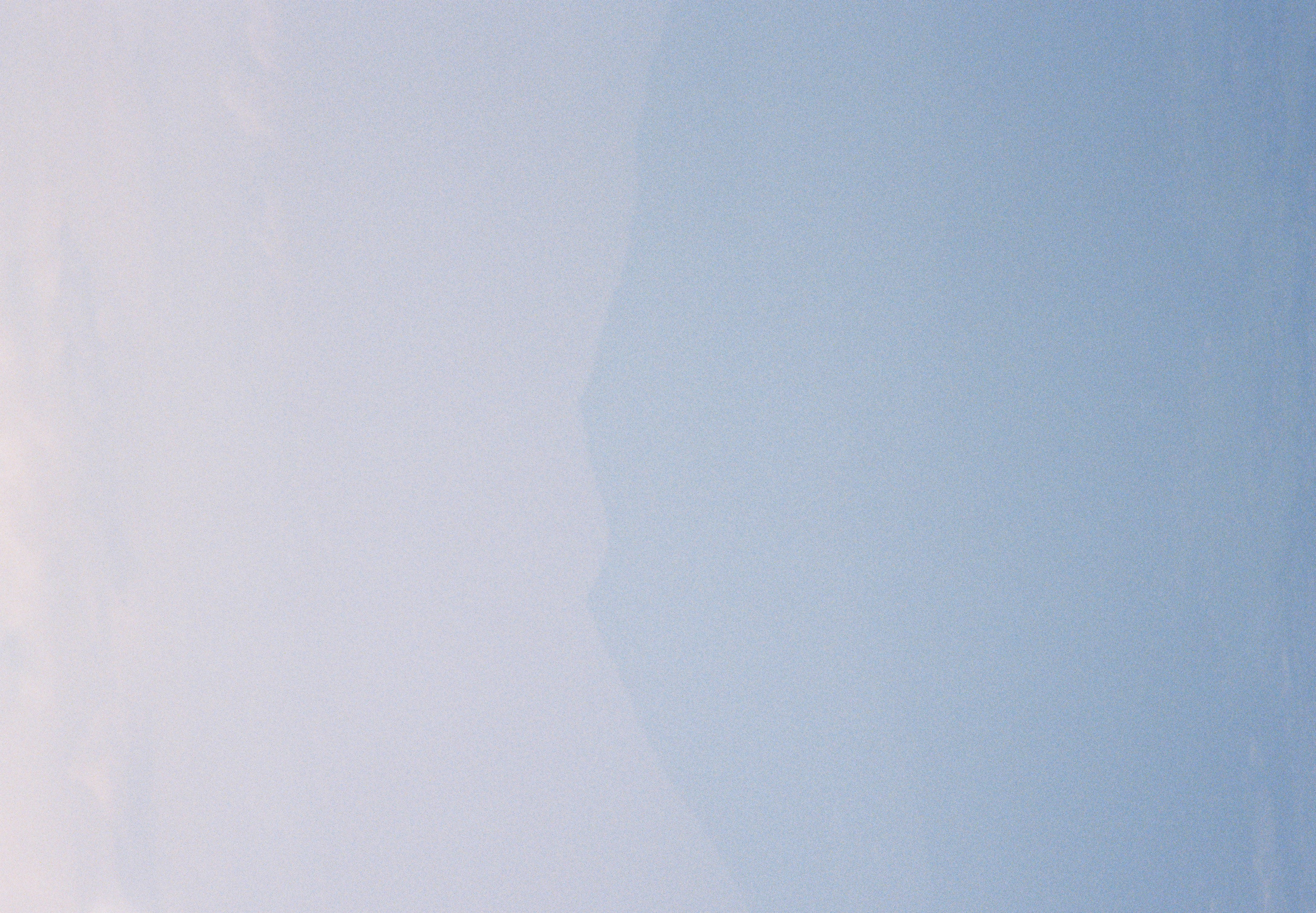 A mountain ridge appears as a faint blue silhouette, nearly dissolved into a pale gradient of haze between sky and slope.