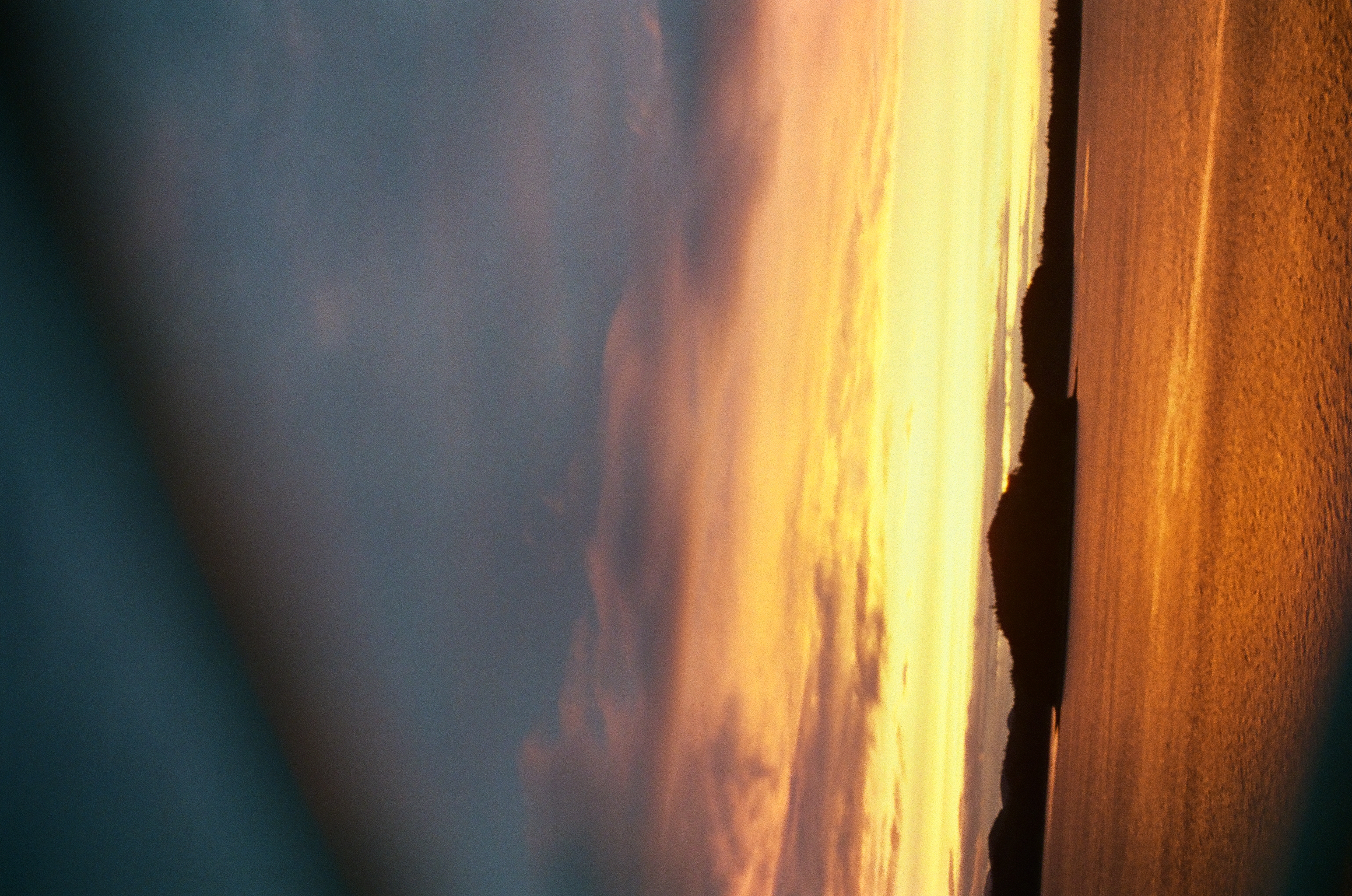 Orange dusk glows between dark clouds and low island silhouettes above softly reflective water.
