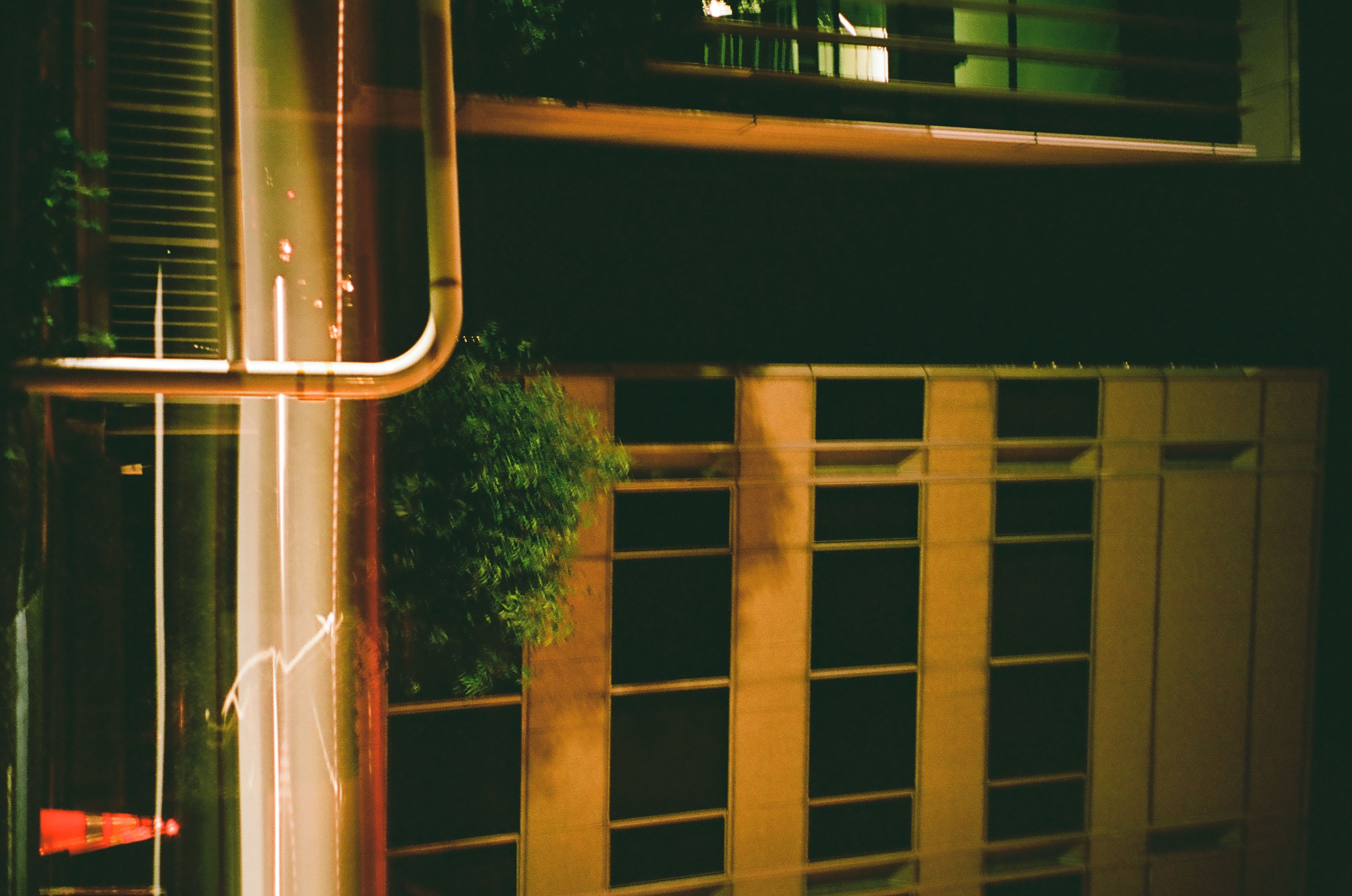 Horizontal light streaks from passing traffic cross below a mid-rise building facade with dark windows, a guardrail and traffic cone in the foreground.