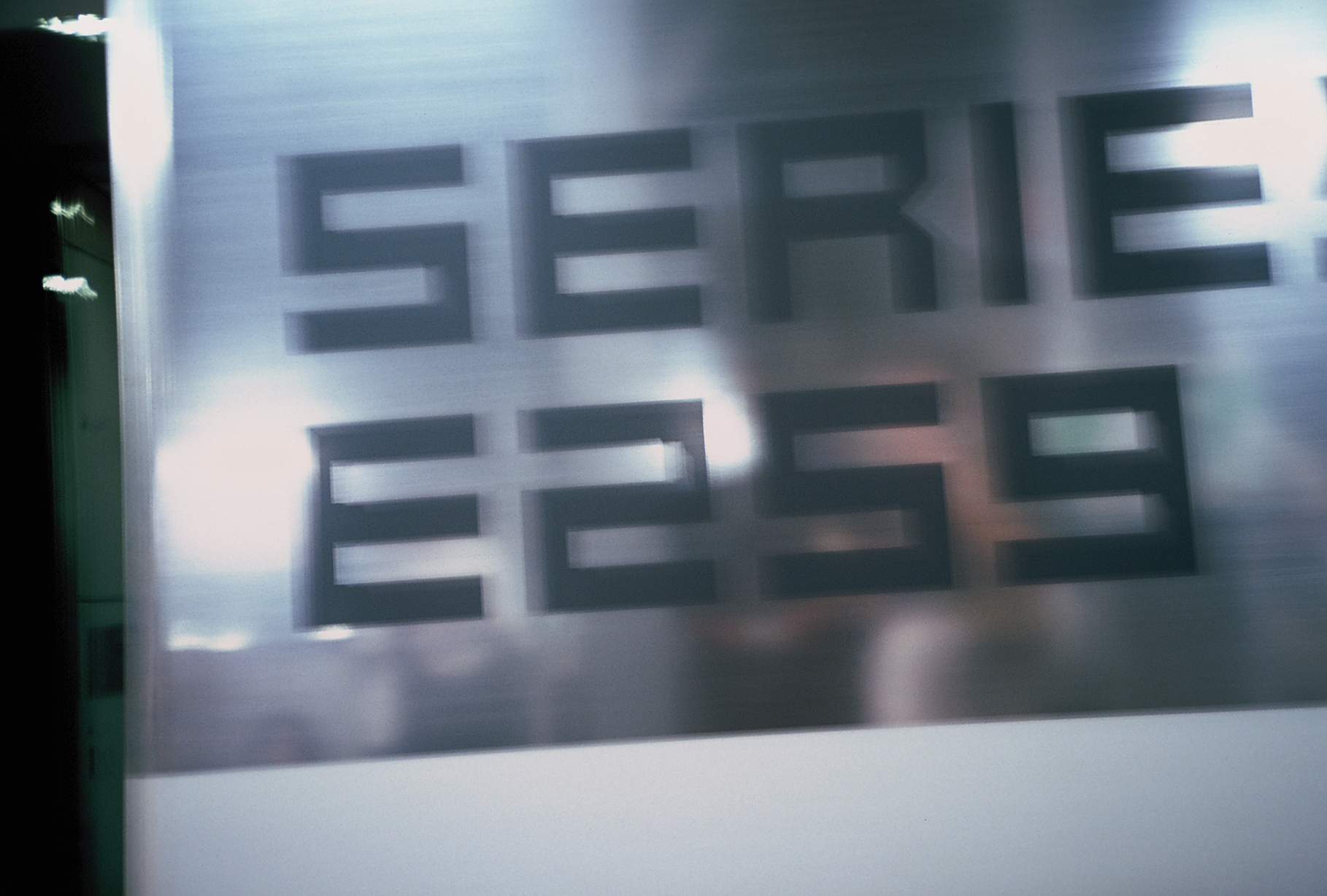 Soft-focus dark lettering reading E259 sits on a brushed metal panel, with a line of larger text cropped above it.