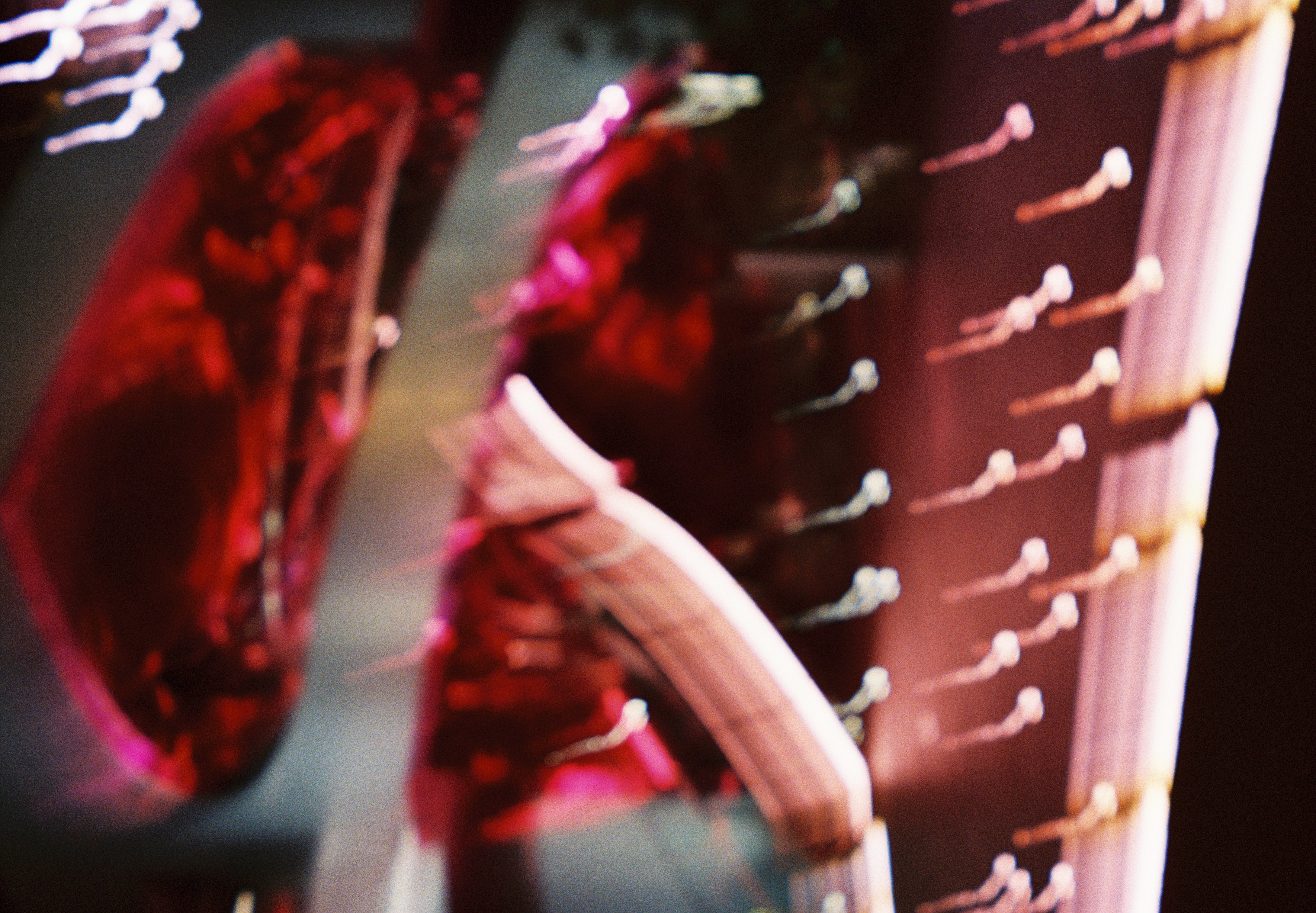 Glossy red illuminated shapes and tiered rows of small light bulbs streak and blur into an abstract pattern of color.