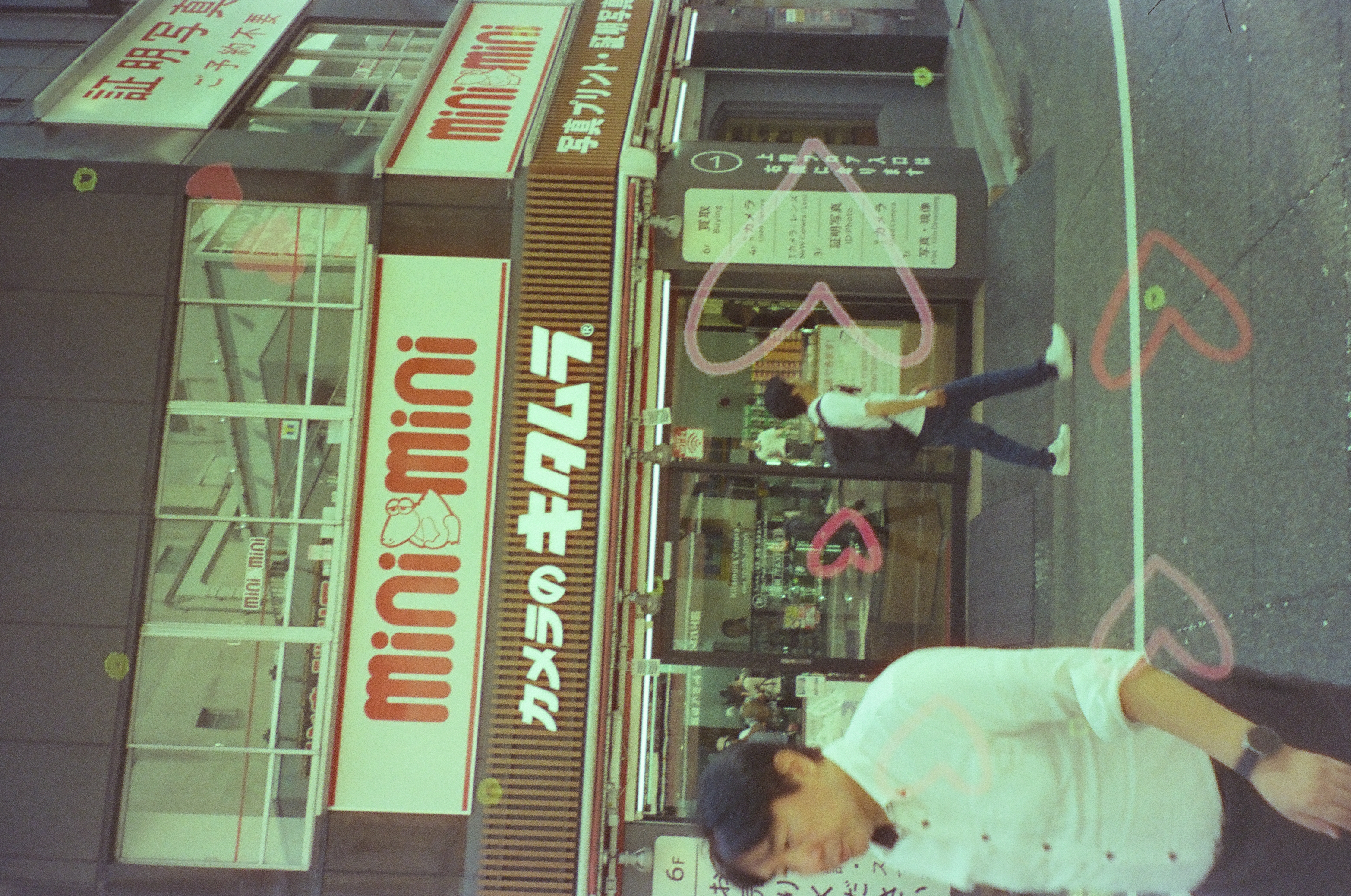 A pedestrian passes a bright storefront while red heart marks trail across the lower glass.
