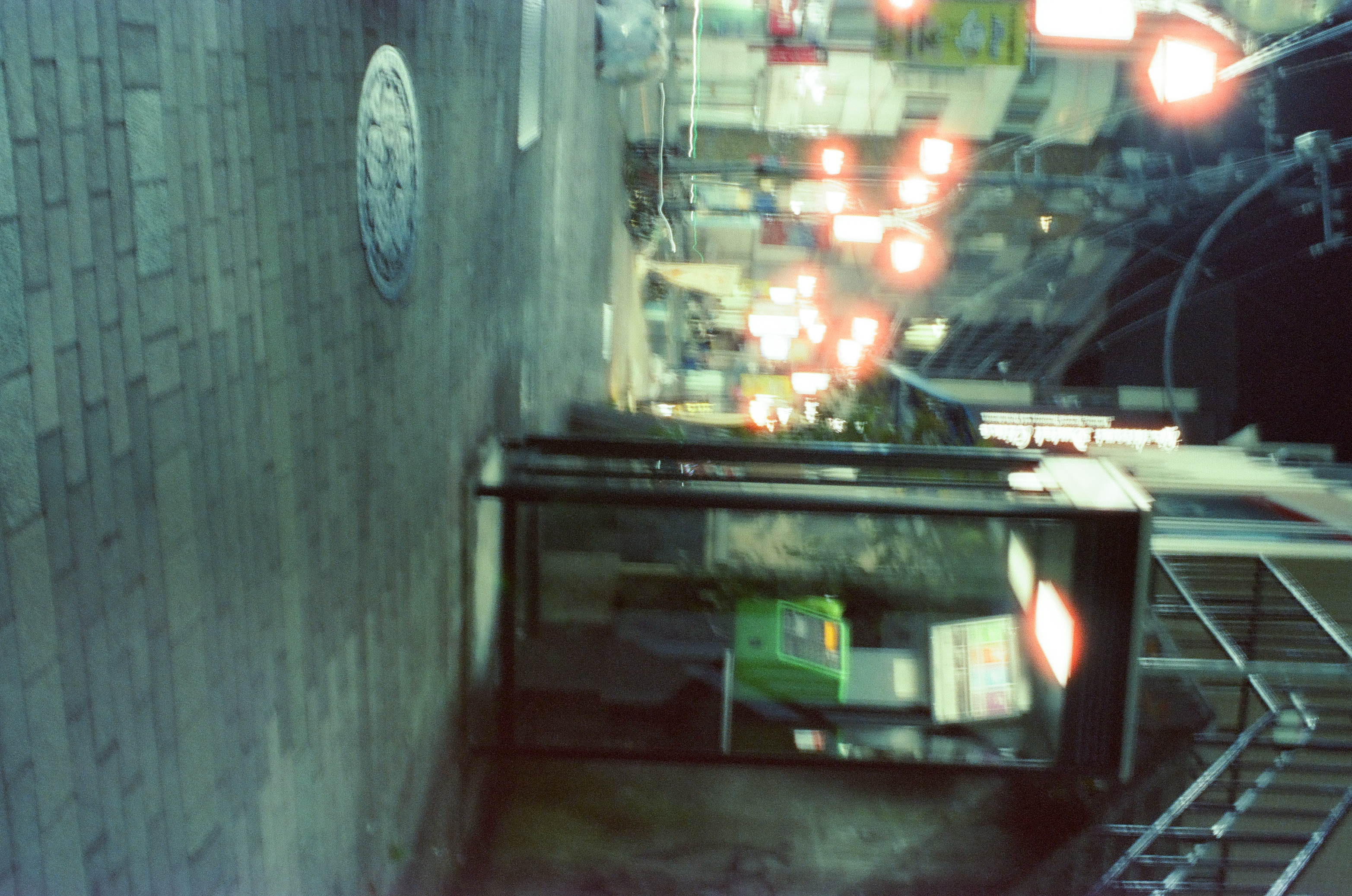 A green public telephone stands beside a narrow night street lined with warm hanging lamps.