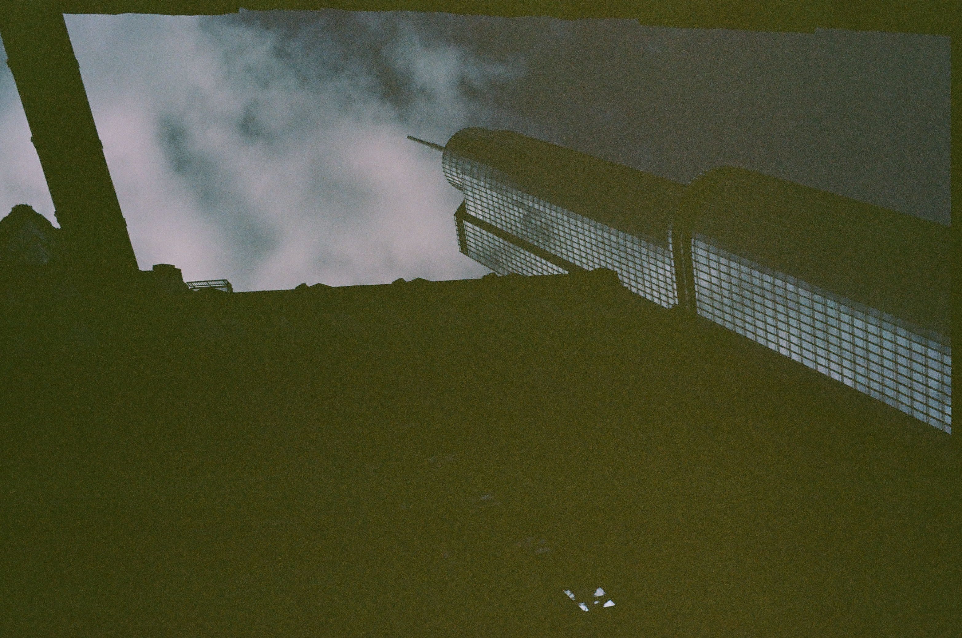 A dark stepped roofline cuts across the lower frame beneath a pale glass tower and cloudy sky.