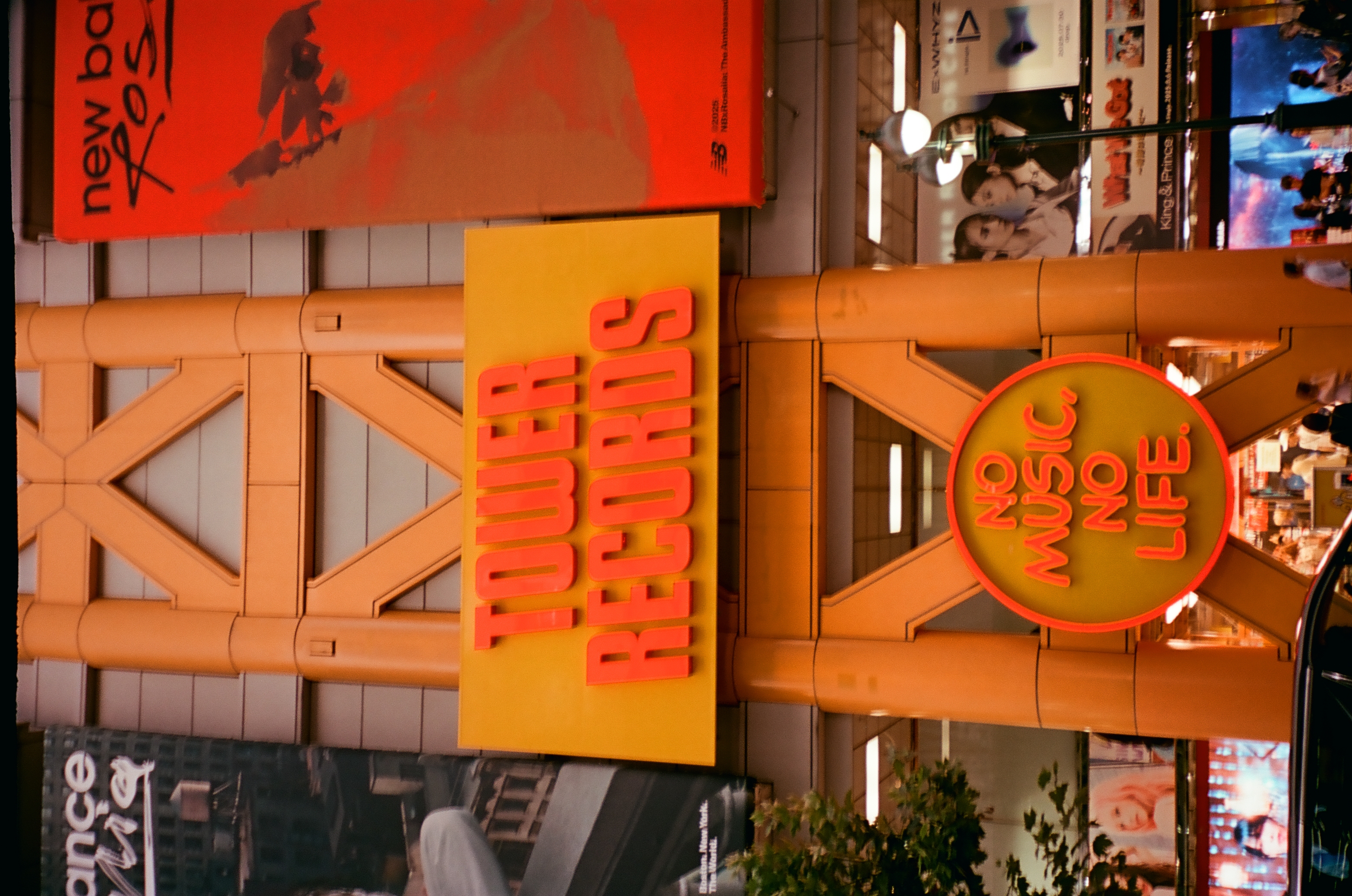 An orange steel lattice frames a yellow Tower Records sign and a round neon sign reading No Music, No Life above a busy sidewalk.