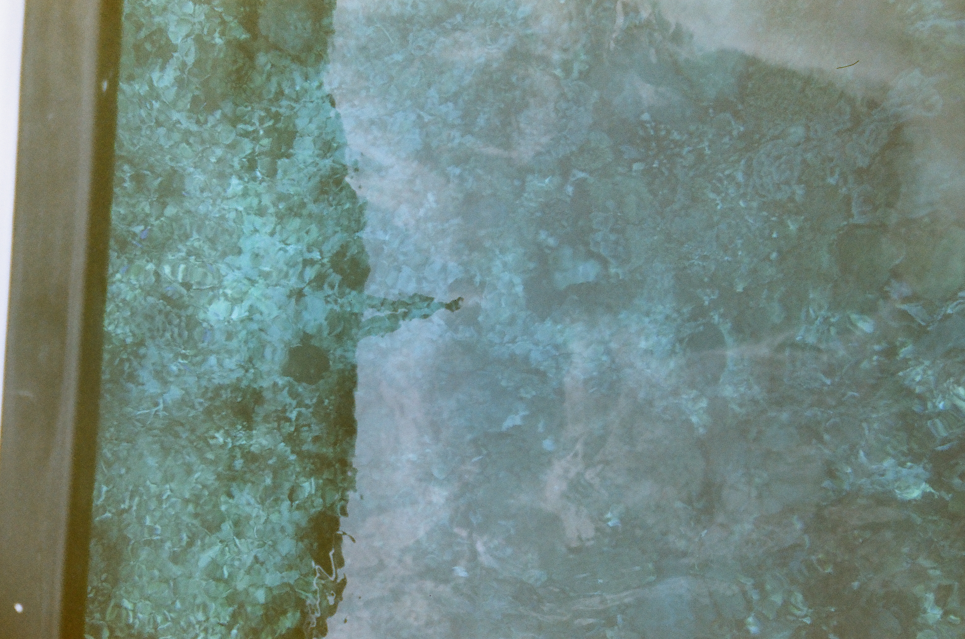 Blue-green wake streams beside the boat through a scratched or weathered window with a narrow wooden edge.
