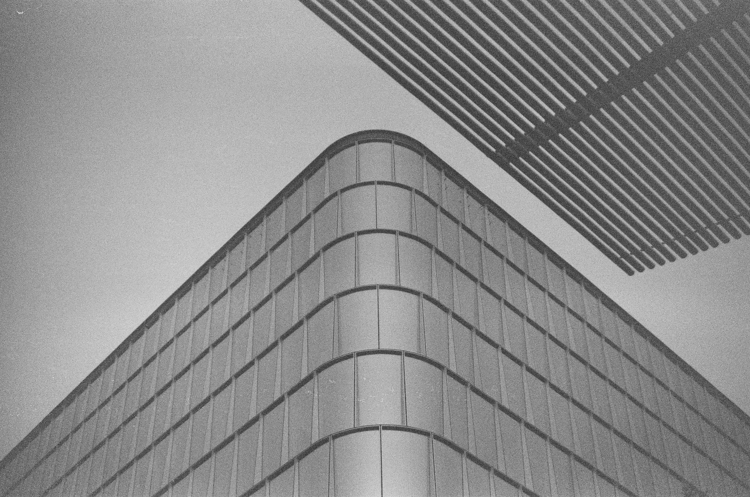 A rounded glass building rises beneath the striped edge of a taller tower against pale sky.