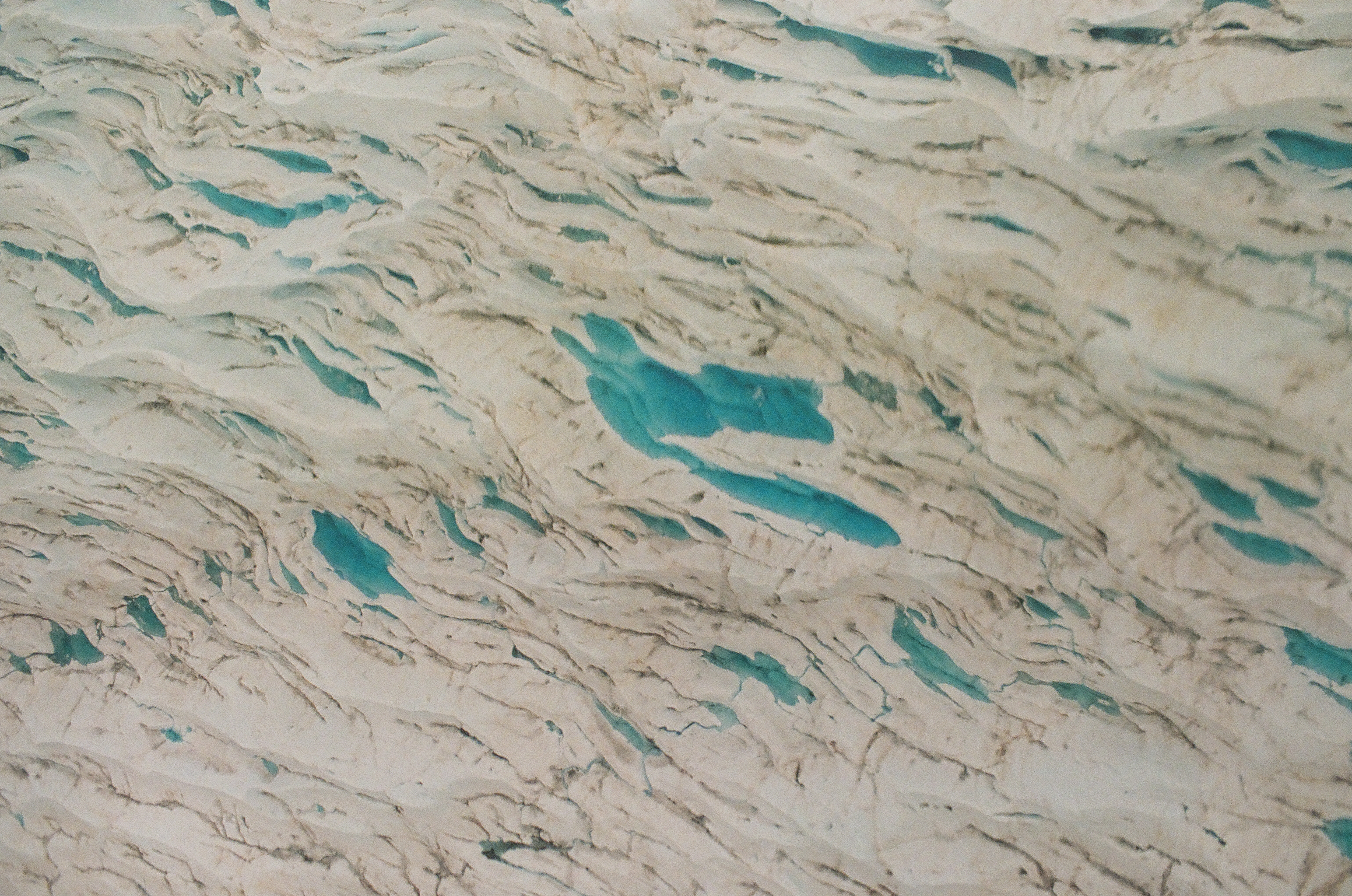 Dense gray crevasses twist across a glacier while vivid blue meltwater gathers in scattered hollows.