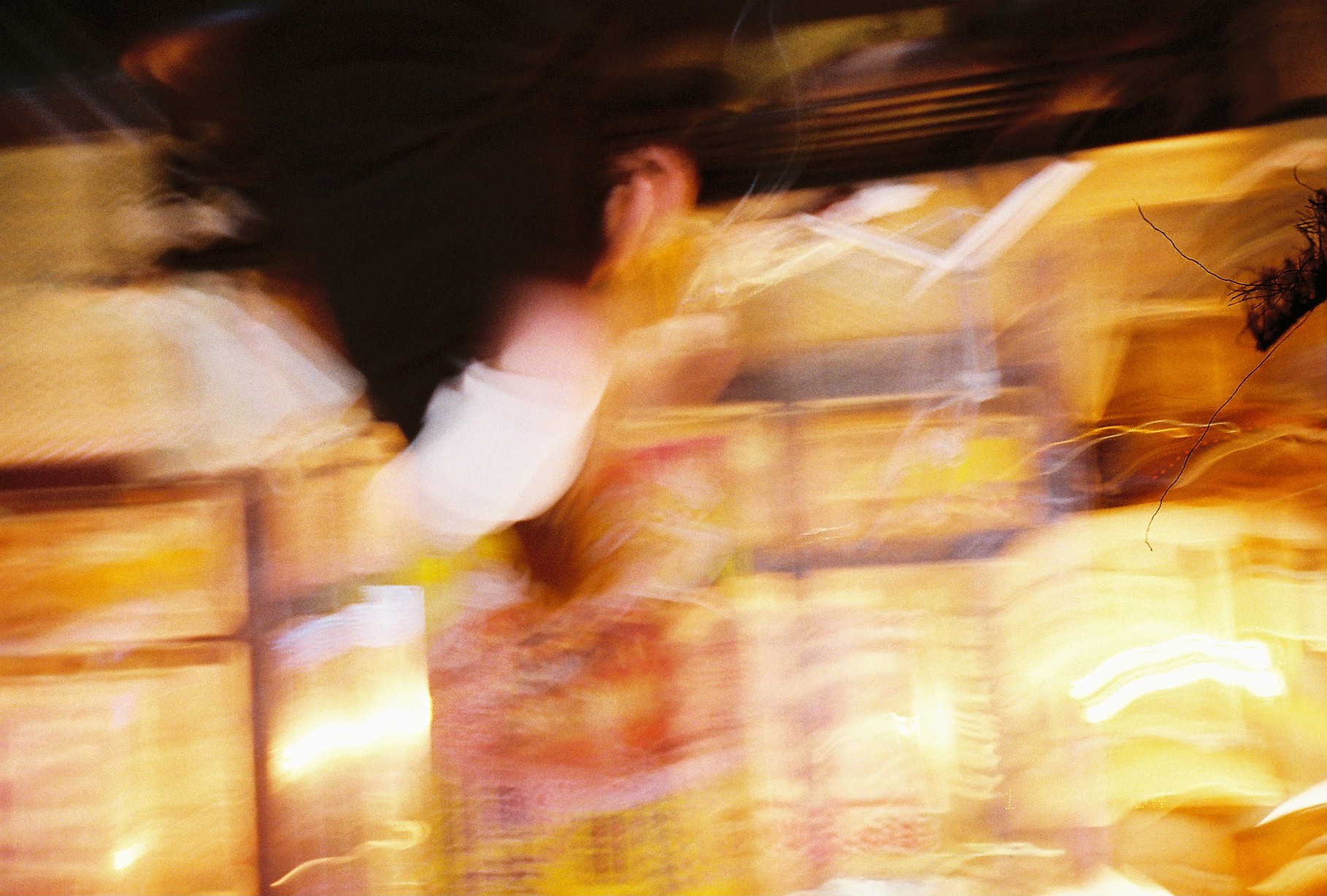 A blurred nighttime exposure shows a figure in a pale top dissolving into streaks of orange and gold signage light.
