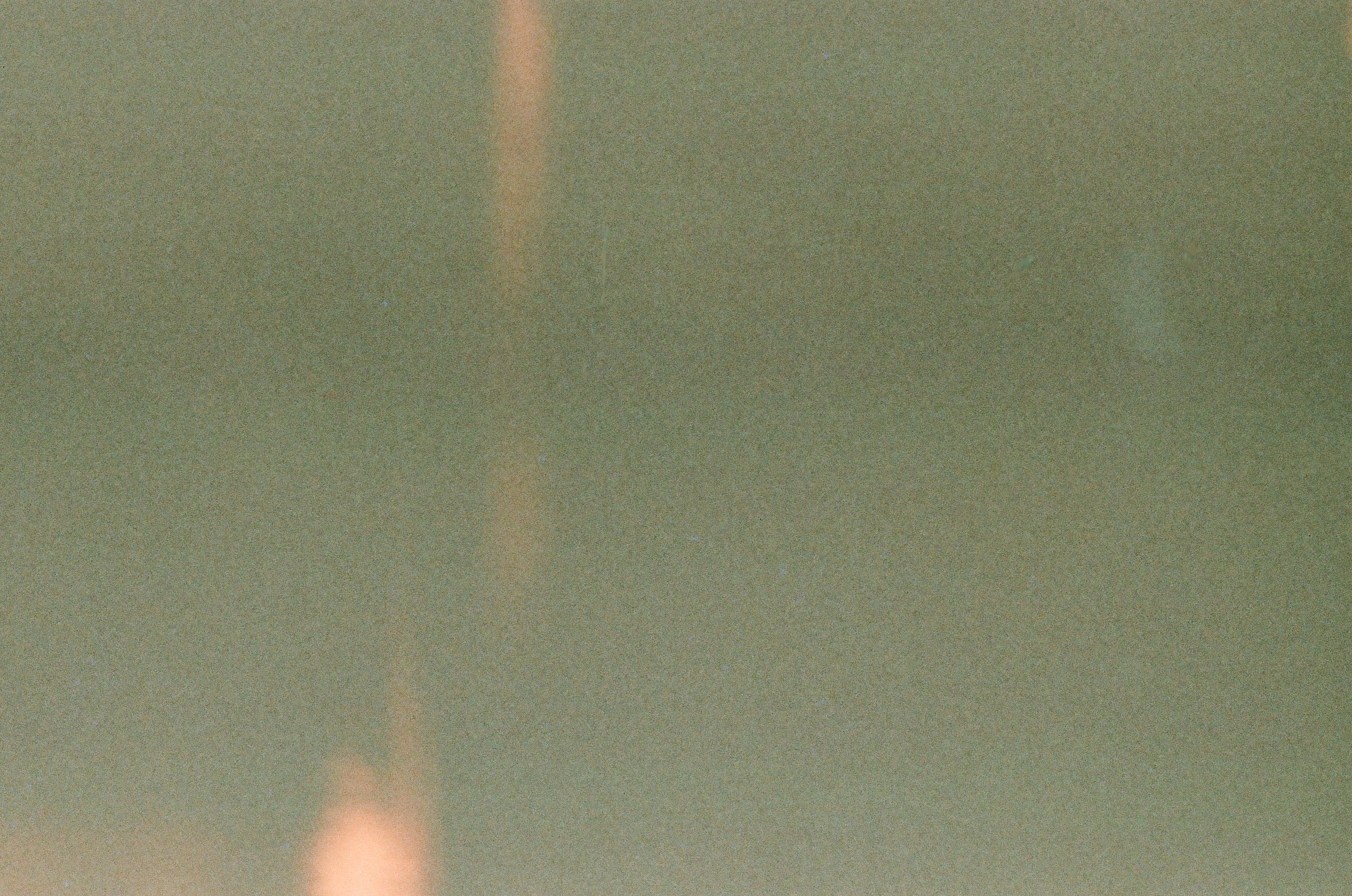A grainy gray-green field is crossed by a faint vertical peach streak ending in a bright bloom at the bottom.