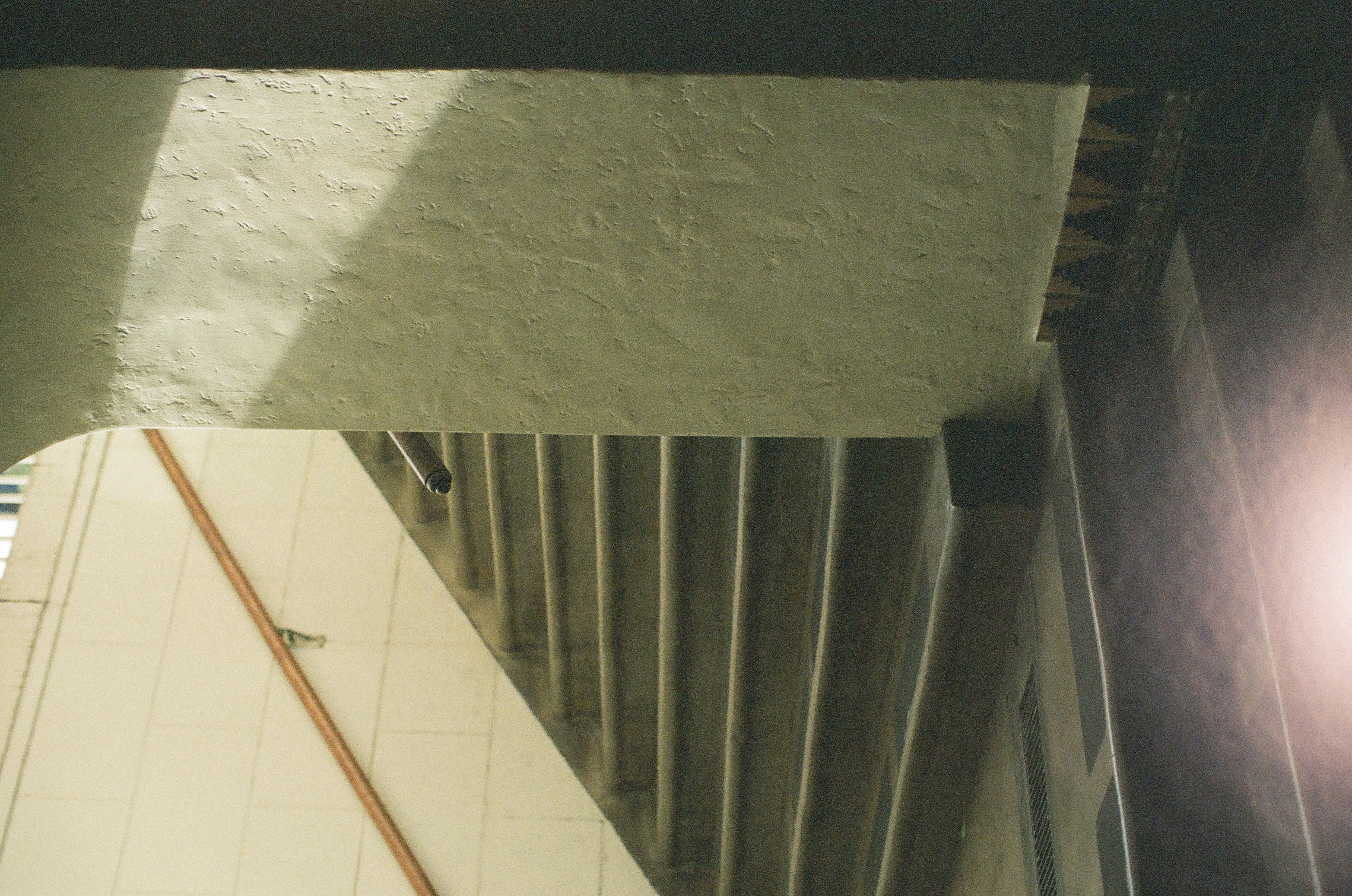 A dark concrete stair turns behind a pale textured wall with a thin metal handrail.