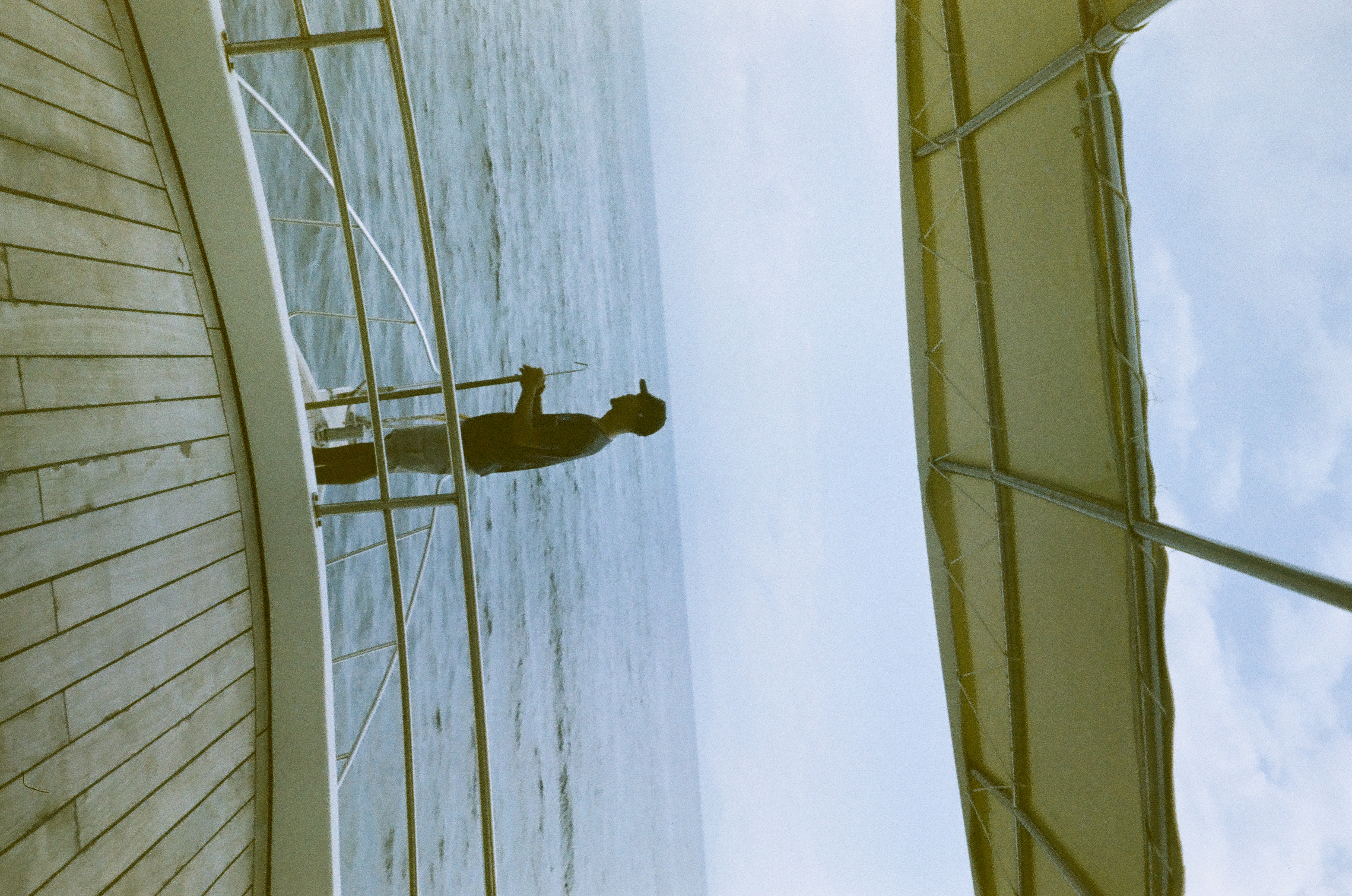 A person stands in profile near the bow rail beneath a canopy with open water extending behind them.