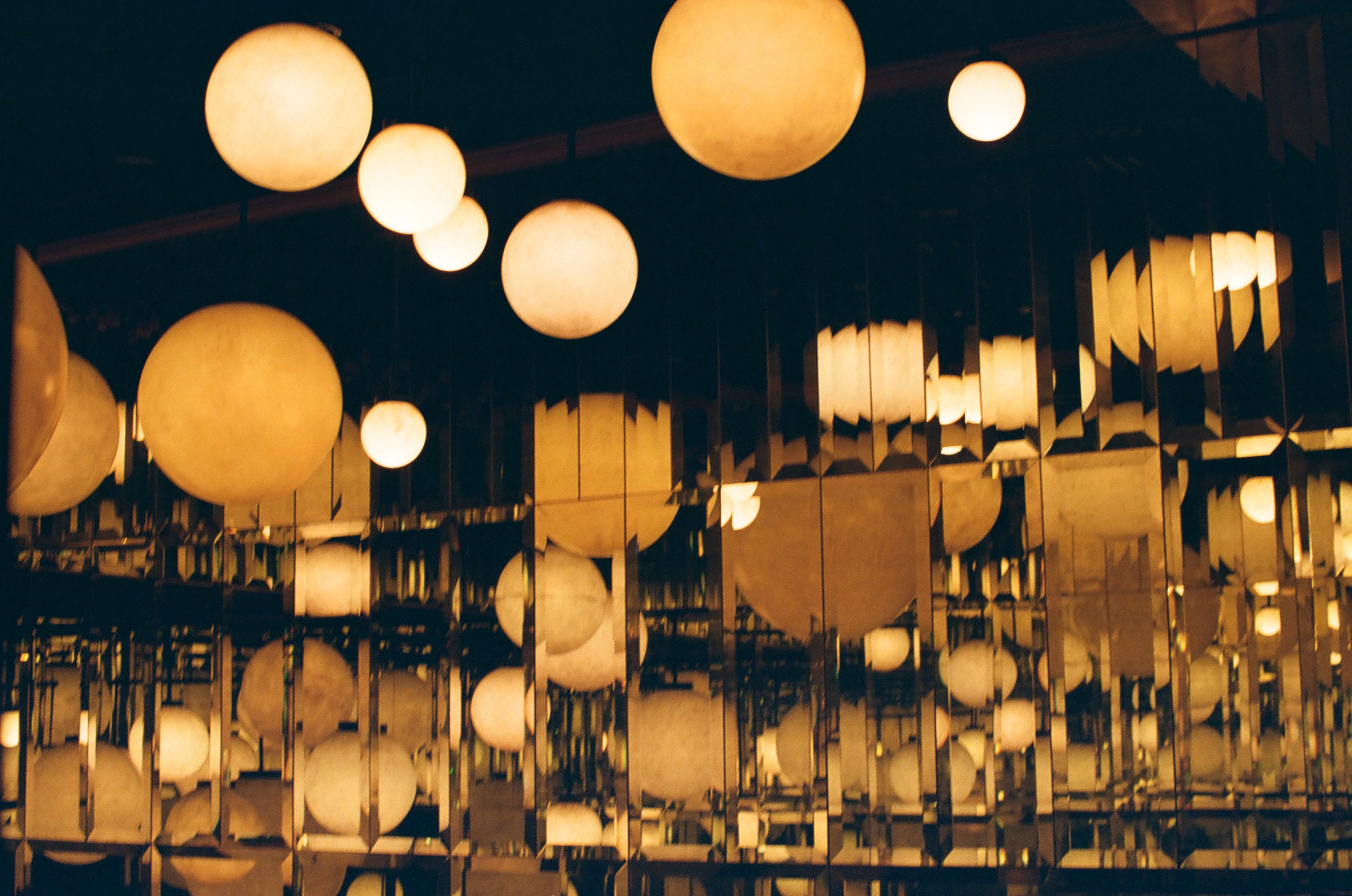 Dozens of round glowing globe lamps repeat in rows across vertical mirrored strips mounted against a dark ceiling.