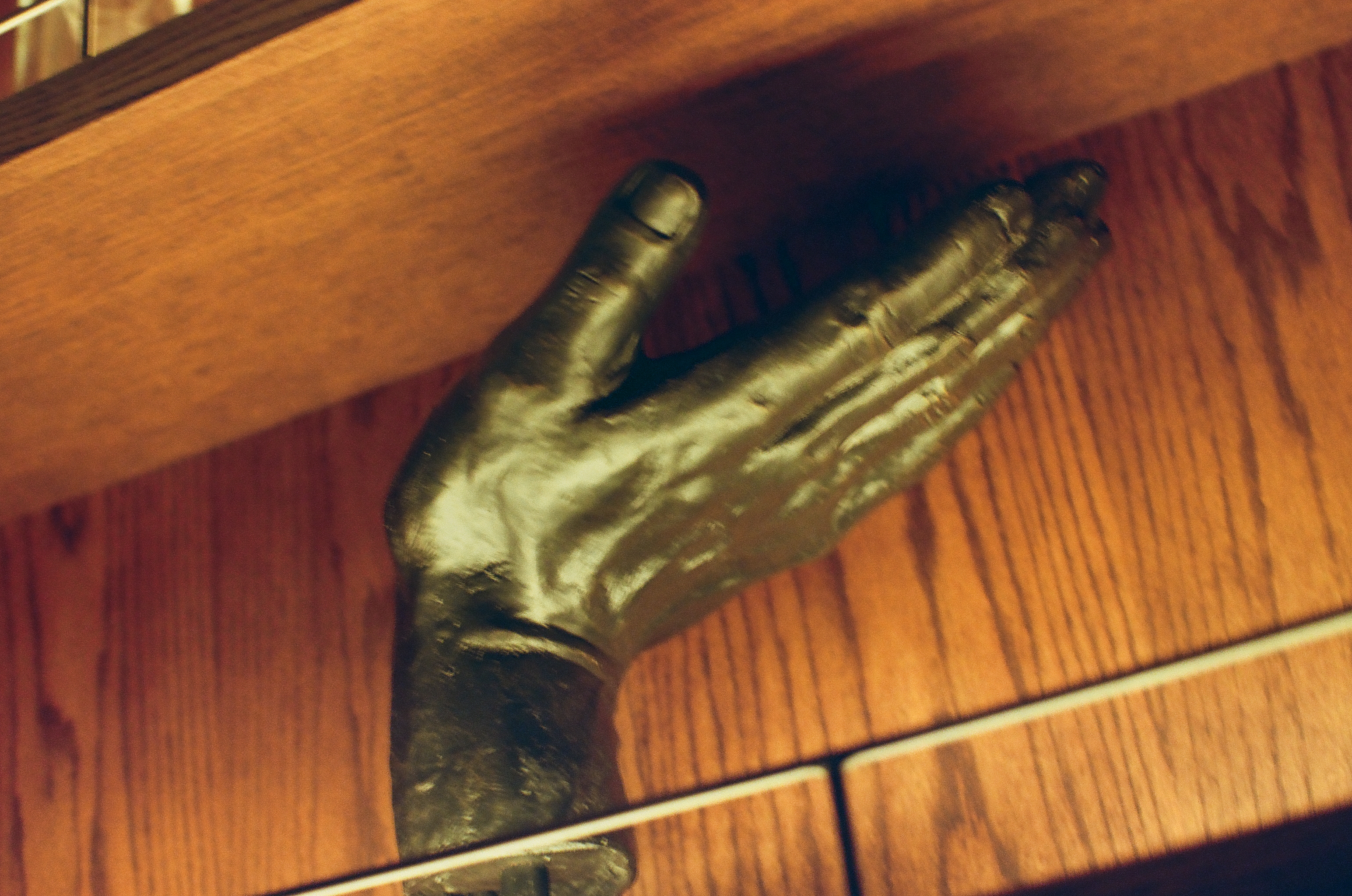 A close view shows the bronze hand sculpture's spread fingers against wood-grain paneling, crossed by a thin metal shelf rail.