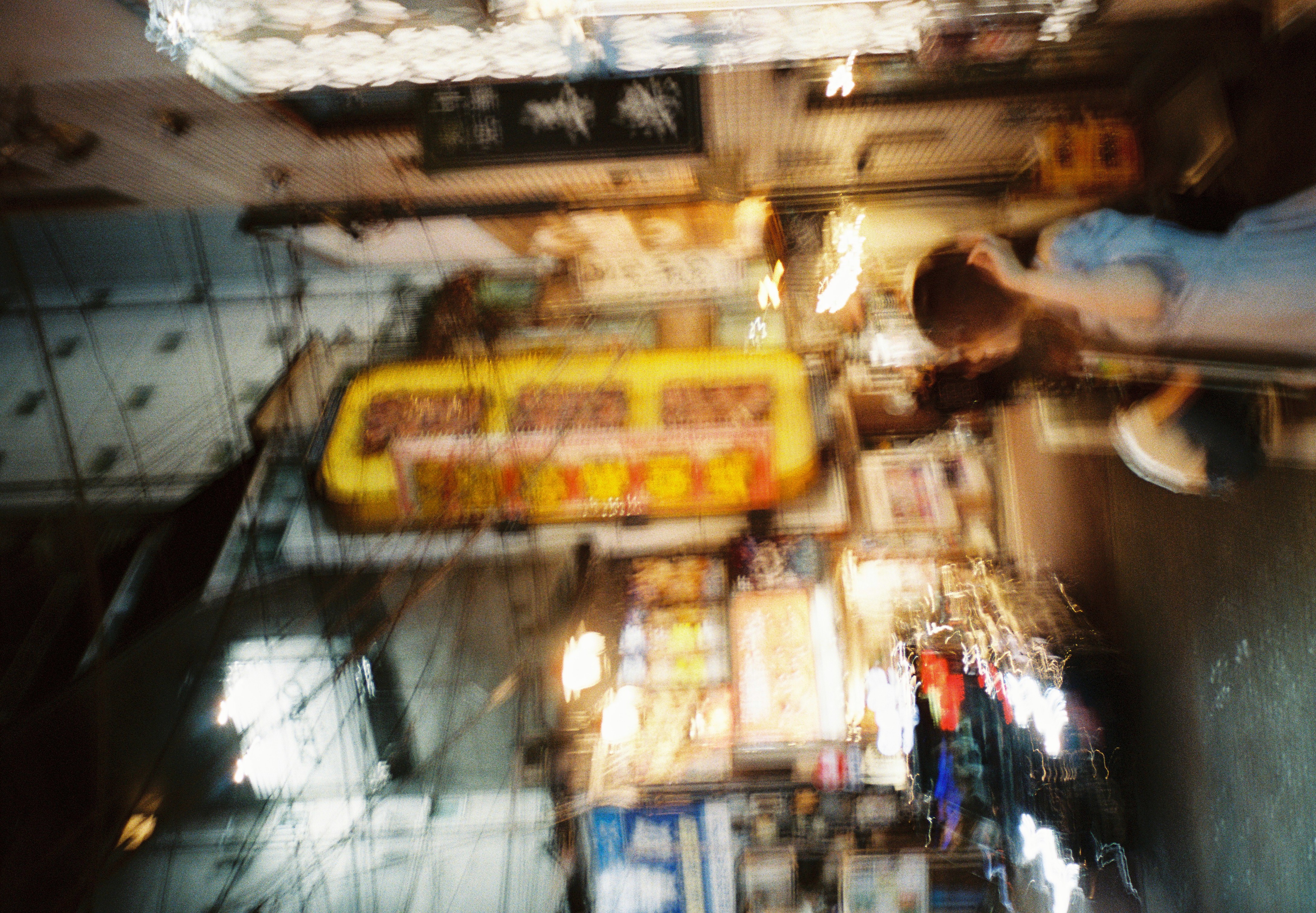 A heavily motion-blurred street scene shows a large yellow vertical sign, overhead wires, and a woman in a pale blue dress.