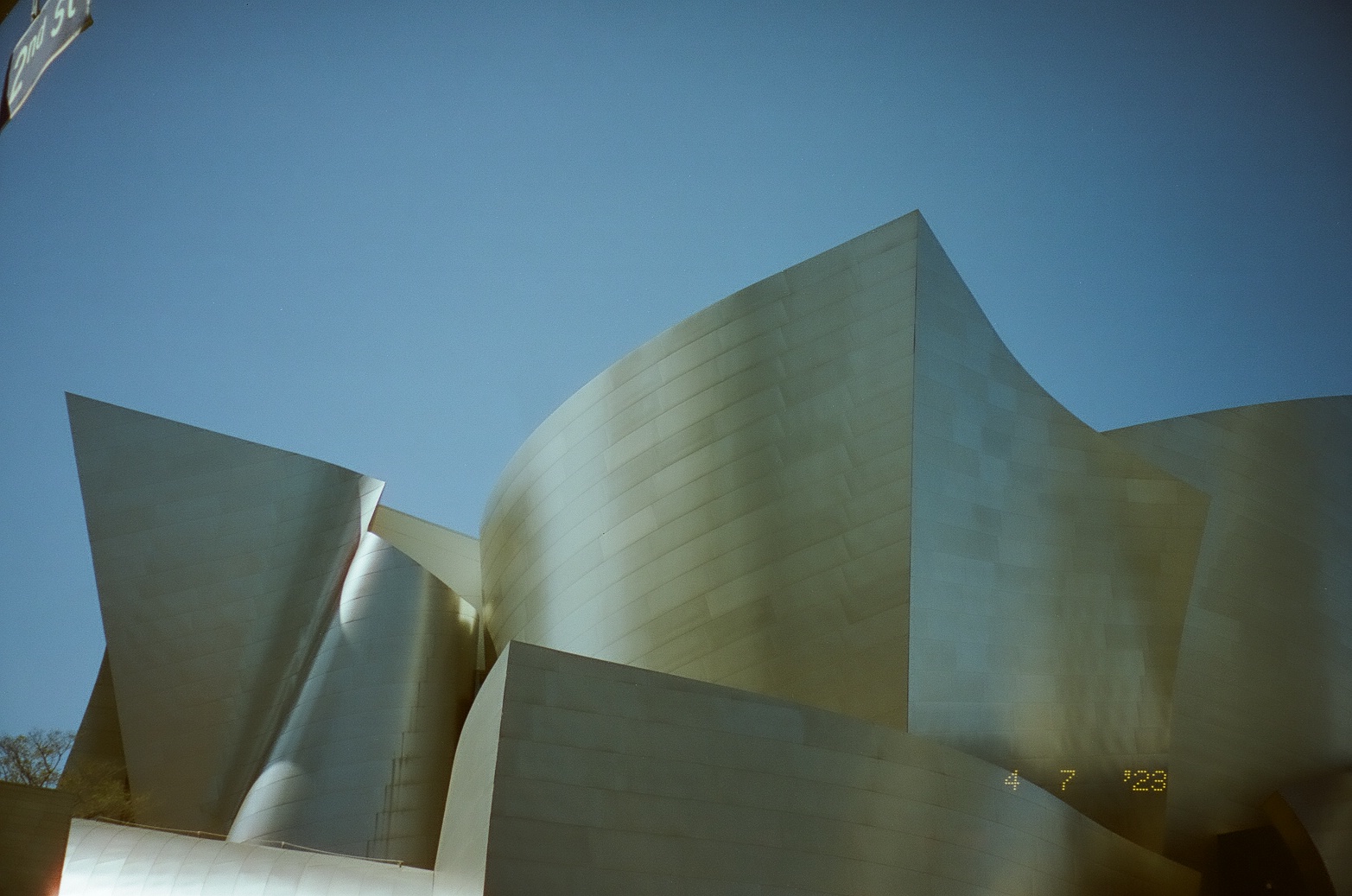 Two sweeping metal facades form a narrow shadowed gap beneath an uninterrupted blue sky.