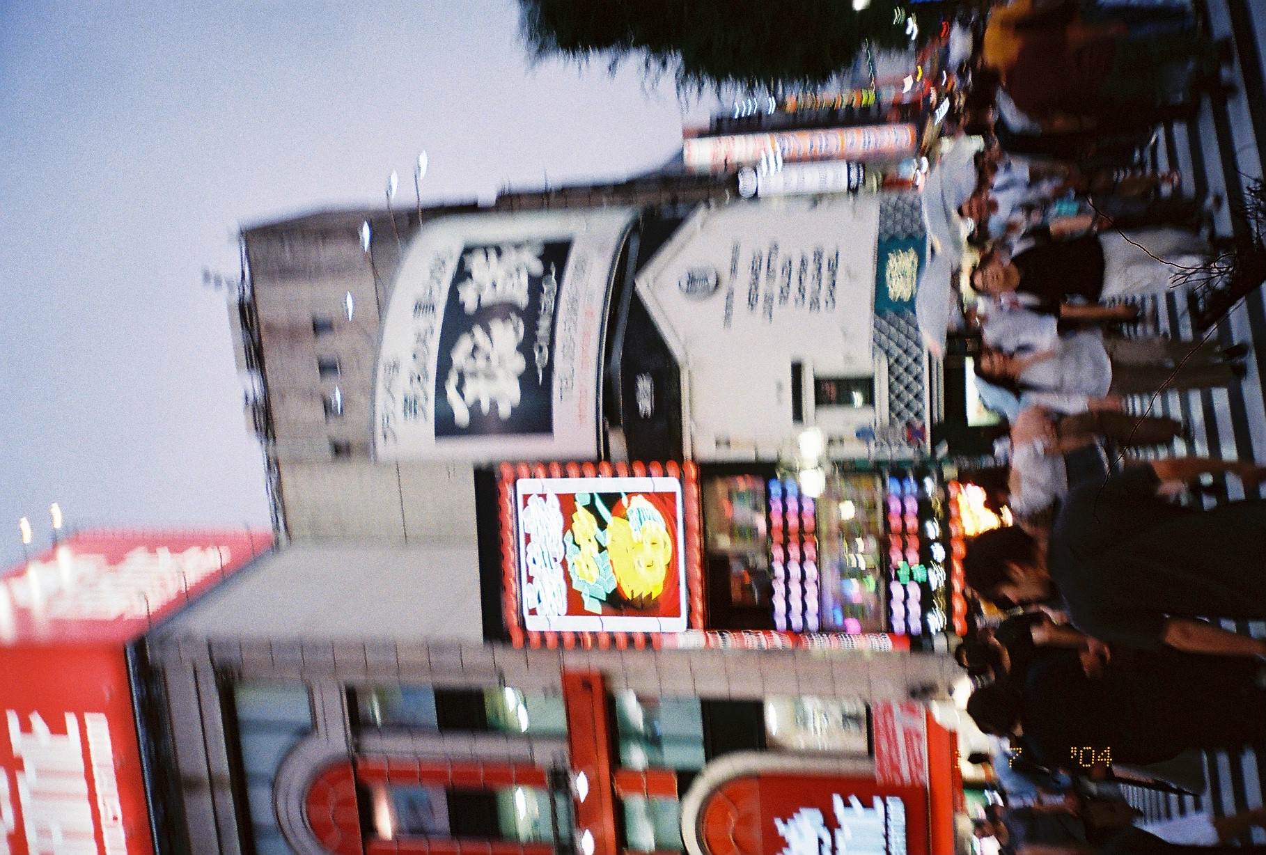 A dense crowd crosses striped pavement beneath tall city facades covered with bright stacked signs.