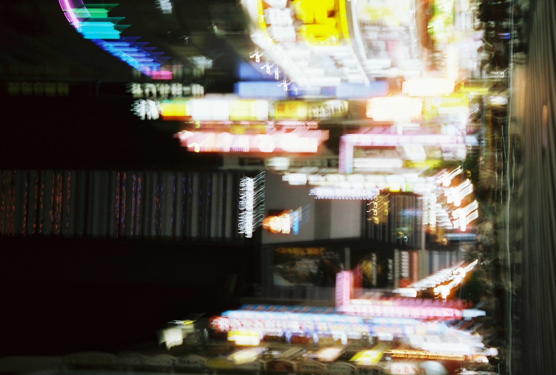 A long exposure smears a neon-lit street into vertical streaks of pink, yellow, and blue, with a sign reading HOTEL GRACERY doubled overhead.