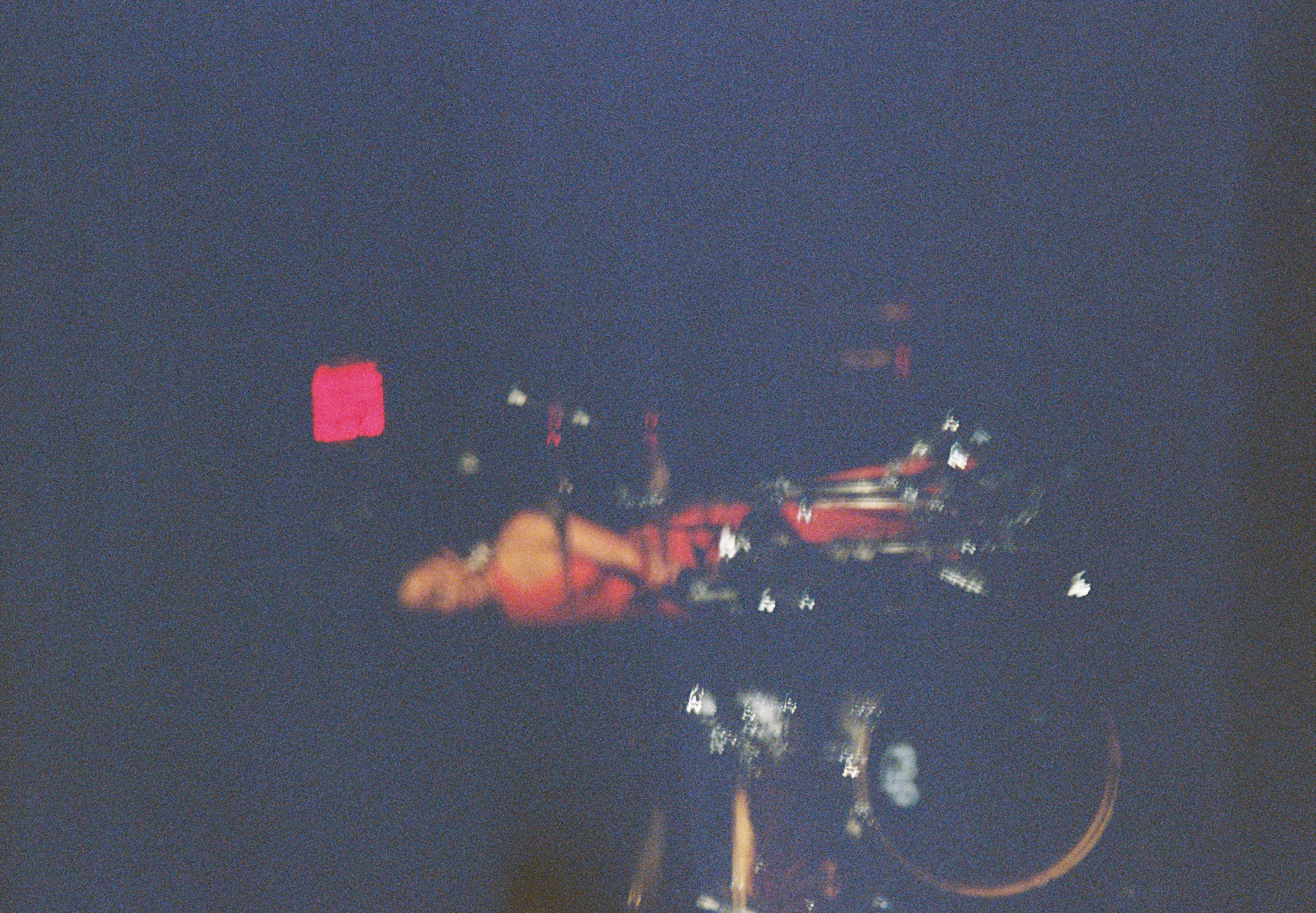 A blurred person stands beside a bicycle beneath a bright red square in deep blue grain.