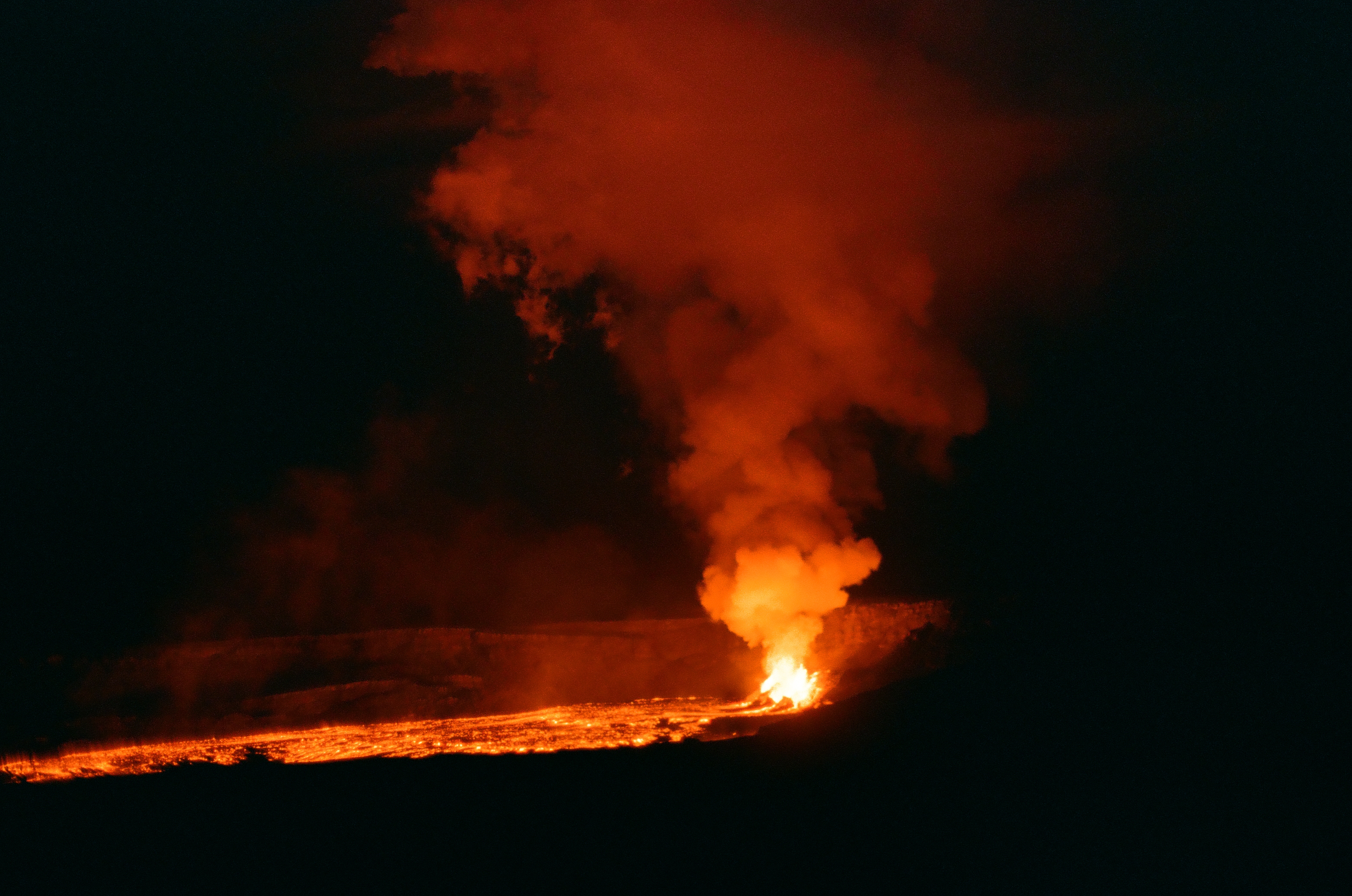 A compact orange vent sends a red-lit plume upward above a thin molten line in darkness.