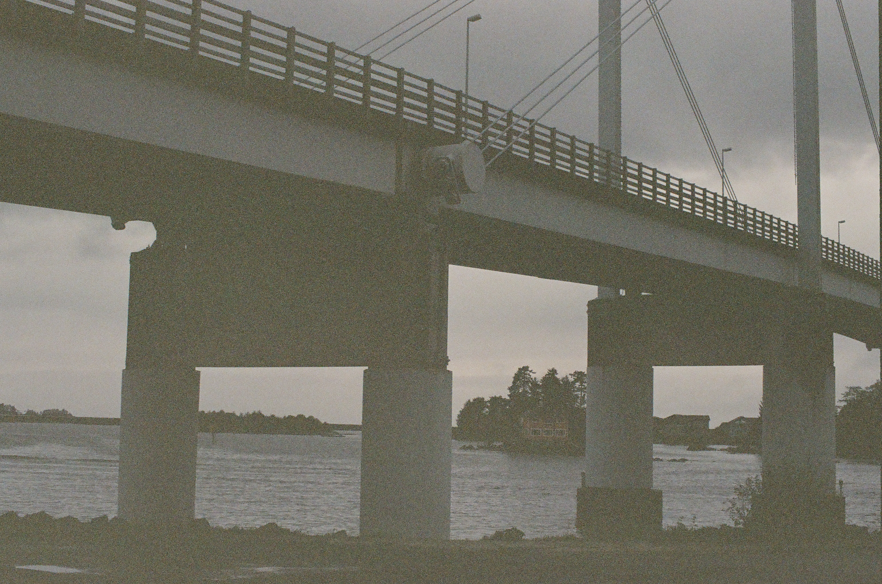 A low bridge crosses gray water on heavy concrete piers beneath an evenly overcast sky.
