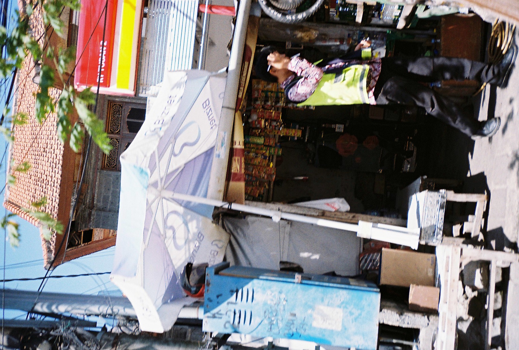 A person in a bright reflective vest raises one hand near their face beside a stall shaded by a broad white umbrella.