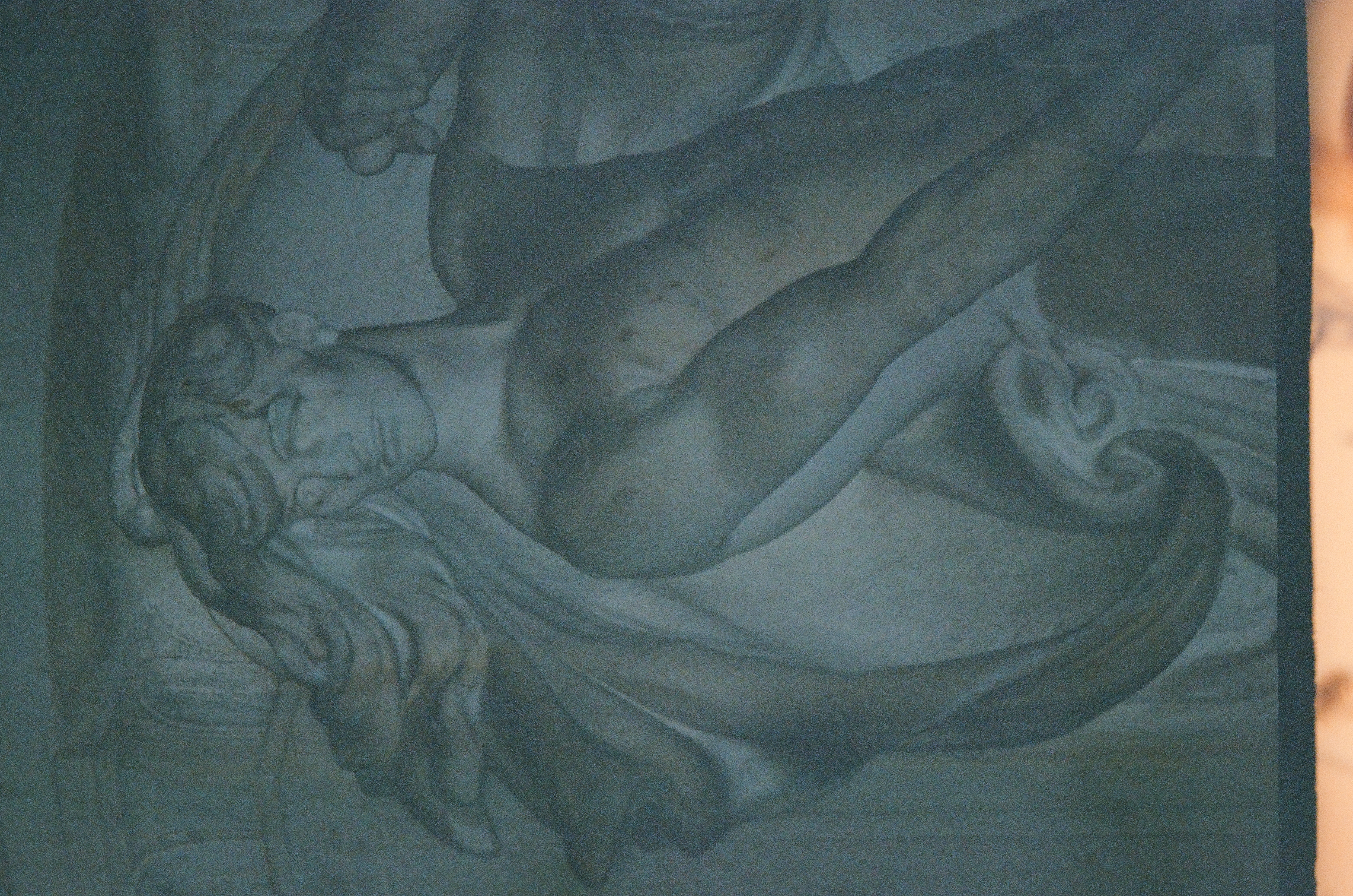 Carved relief of a muscular figure with flowing hair and swirling drapery, one arm raised, beneath a flat horizontal band with column-like forms at the upper left.