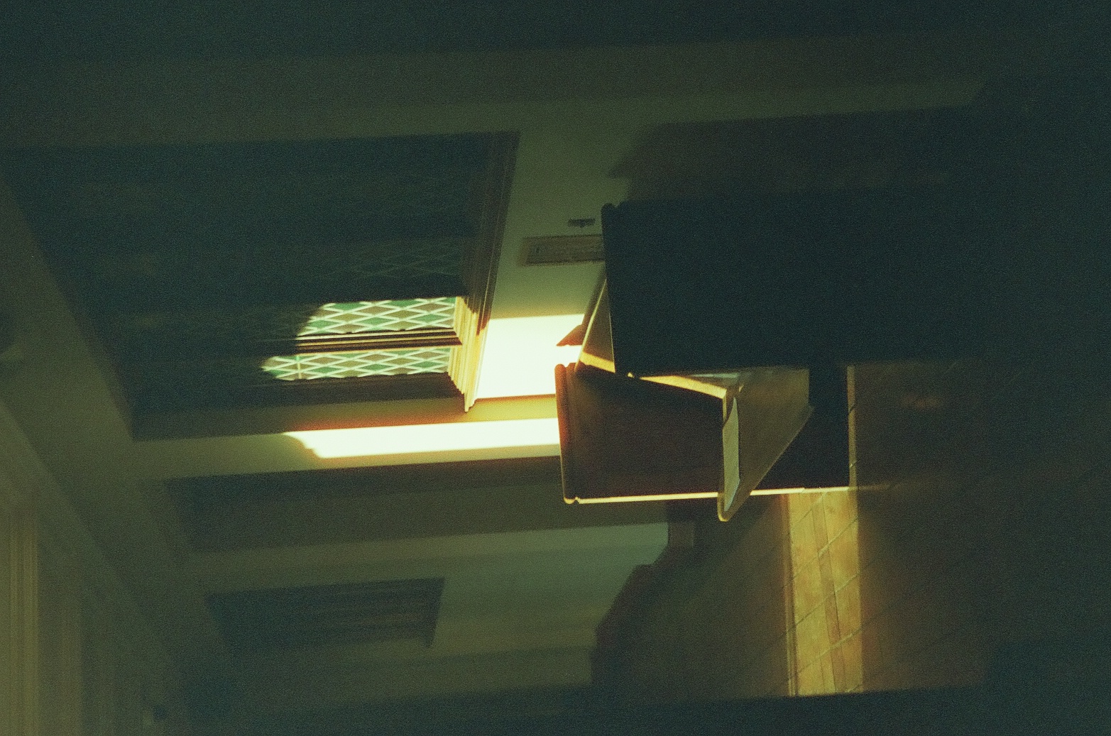 A wooden chair and dark lectern stand in a quiet tiled aisle pierced by a narrow rectangle of sunlight.