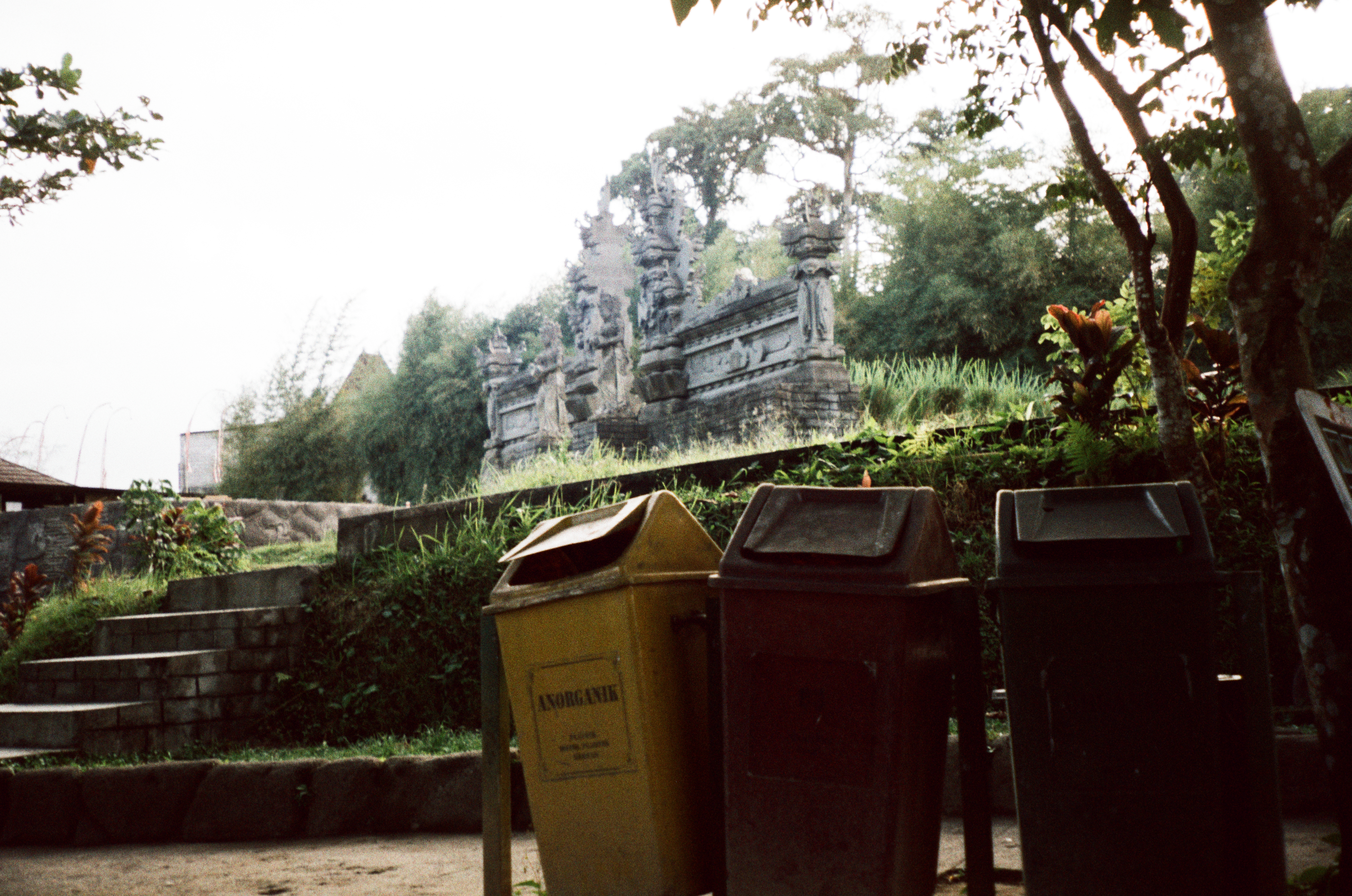 Yellow, reddish-brown, and dark green bins fill the foreground below gray steps and a carved gray structure; “ANORGANIK” is readable on the yellow bin.
