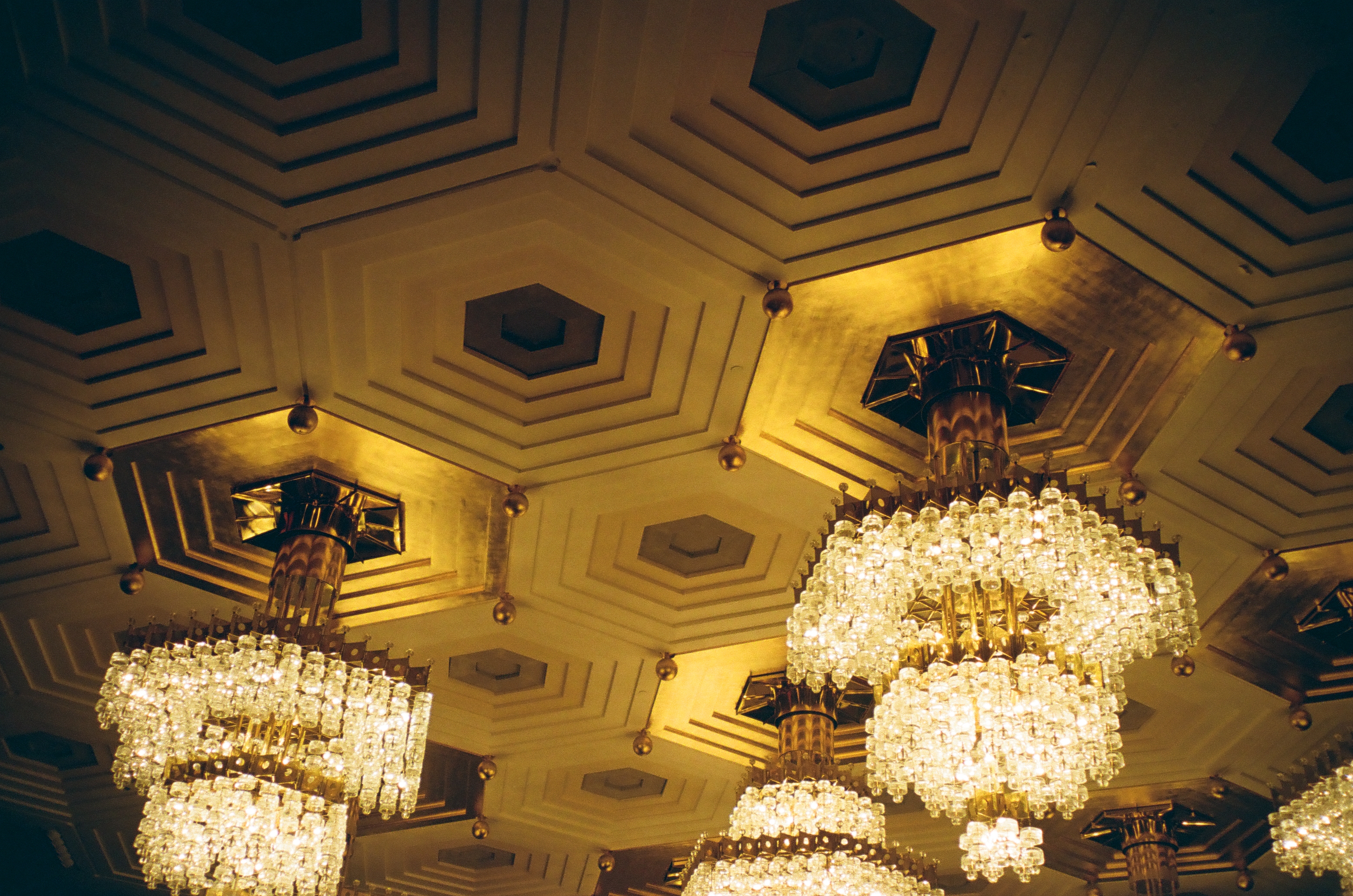 Several crystal chandeliers glow beneath a deeply patterned ceiling of repeated geometric panels.