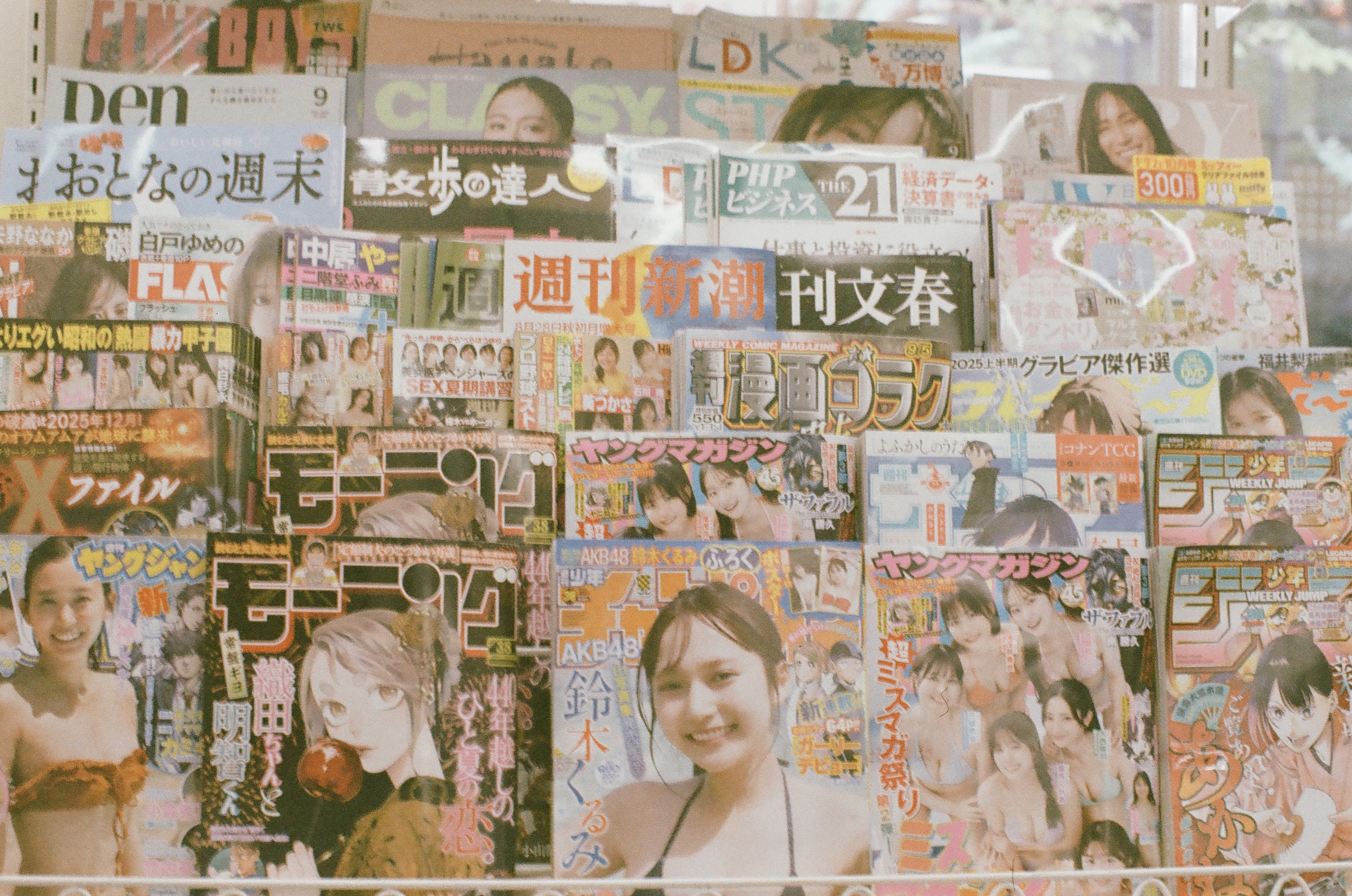 Rows of Japanese-language magazine and manga covers, some showing women in swimwear, fill a glass-fronted rack from floor to ceiling.