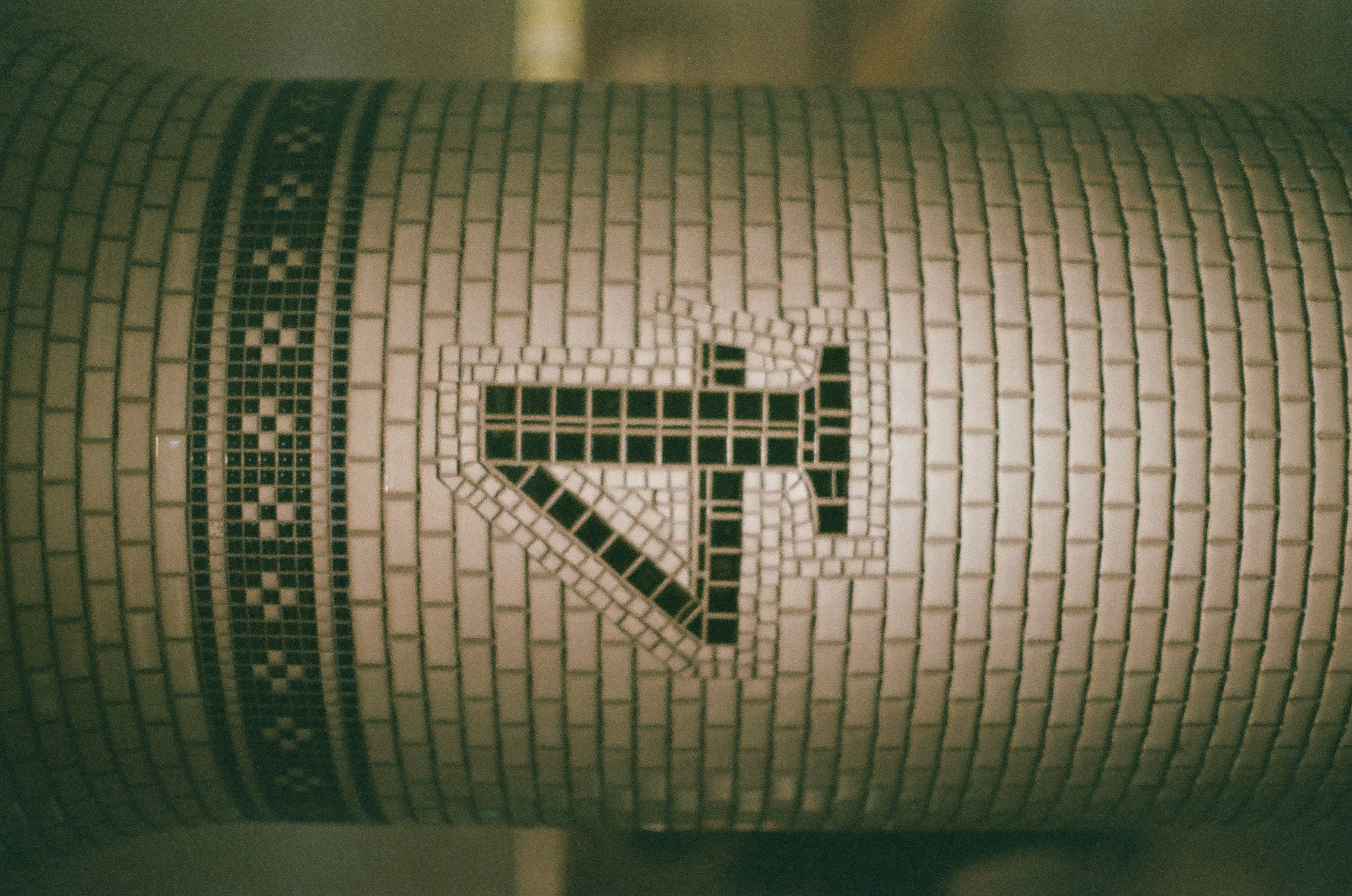 A tiled column shows the numeral four formed from dark mosaic tesserae in an angular shape beneath a checkered band, against plain glazed tile.
