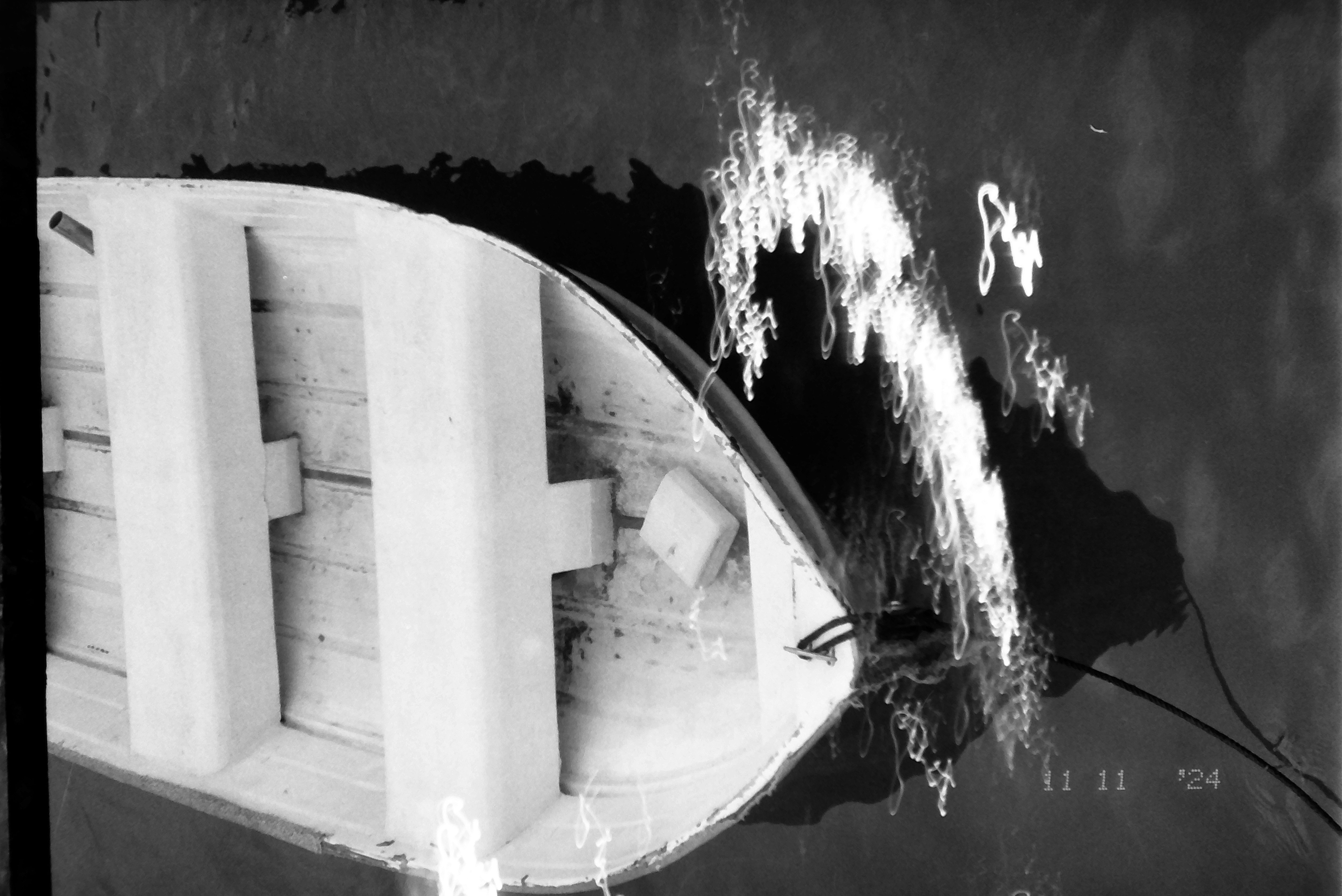 A white wooden rowboat with two bench seats and a mooring line floats on dark water, its bow closest to the camera.
