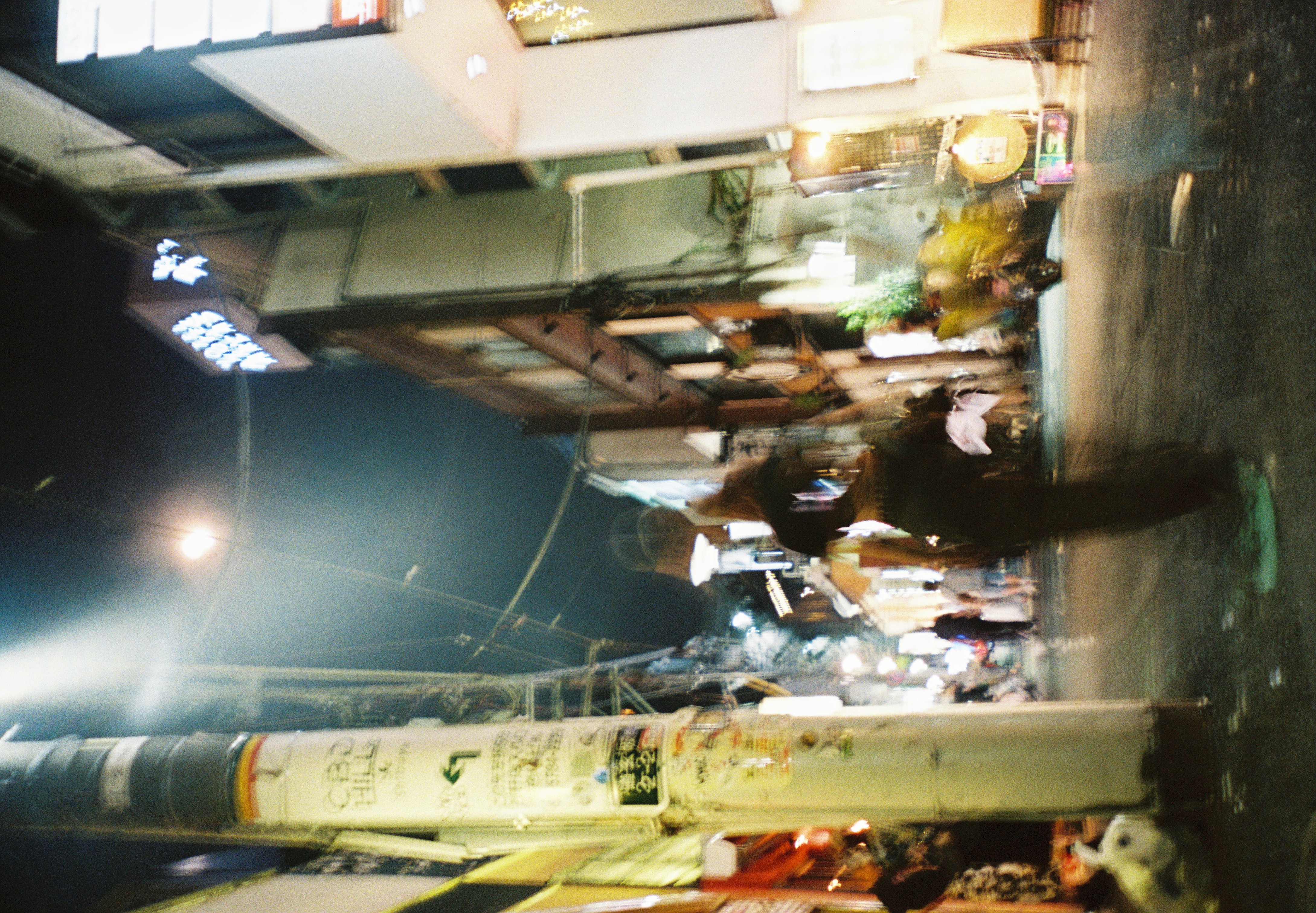 A motion-blurred person walks down a narrow street past a sticker-covered utility pole lettered 'CBD HILL' near its top.