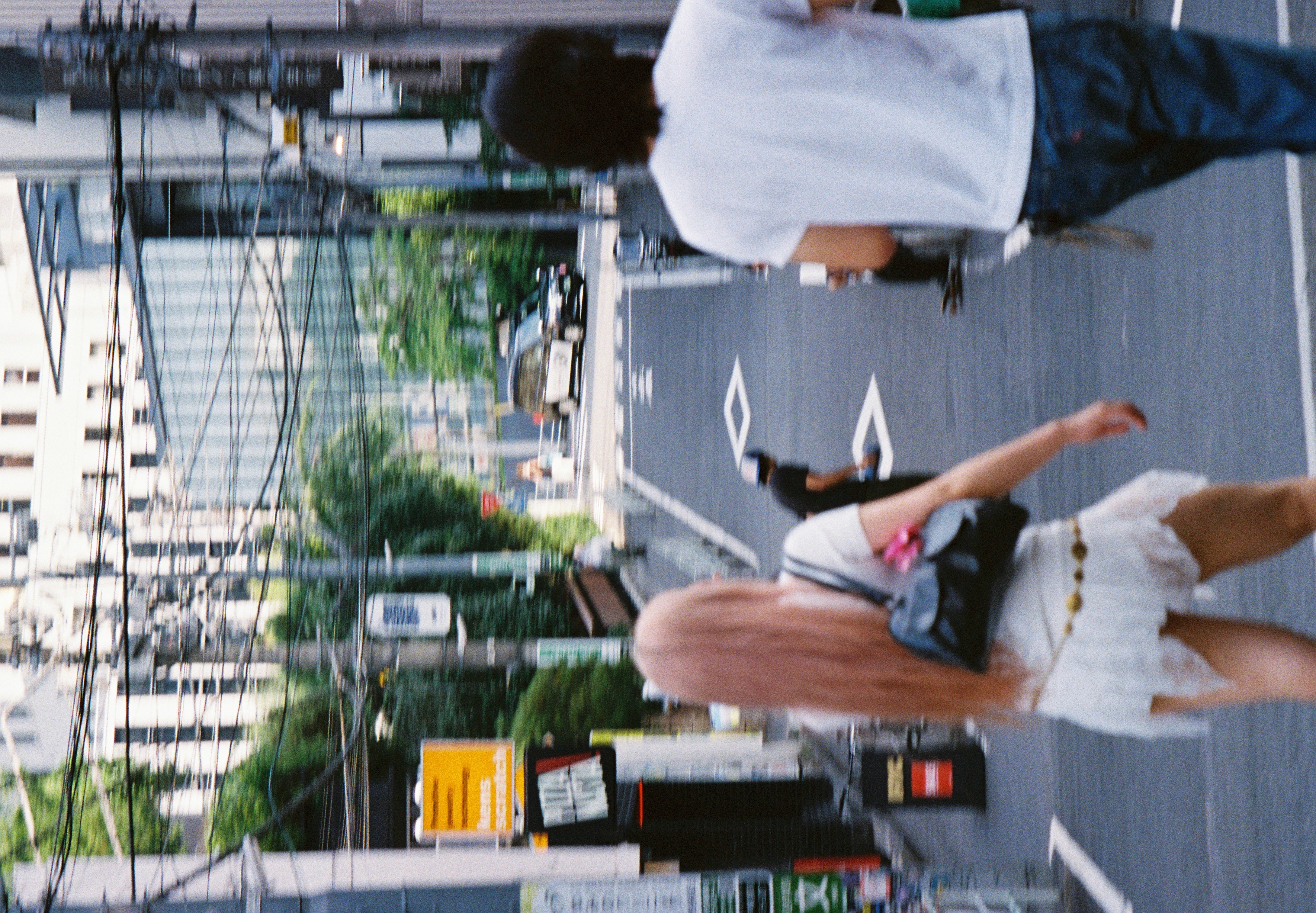 Two people walk away down a sloping street strung with overhead power lines, as a car waits near the bottom of the hill.
