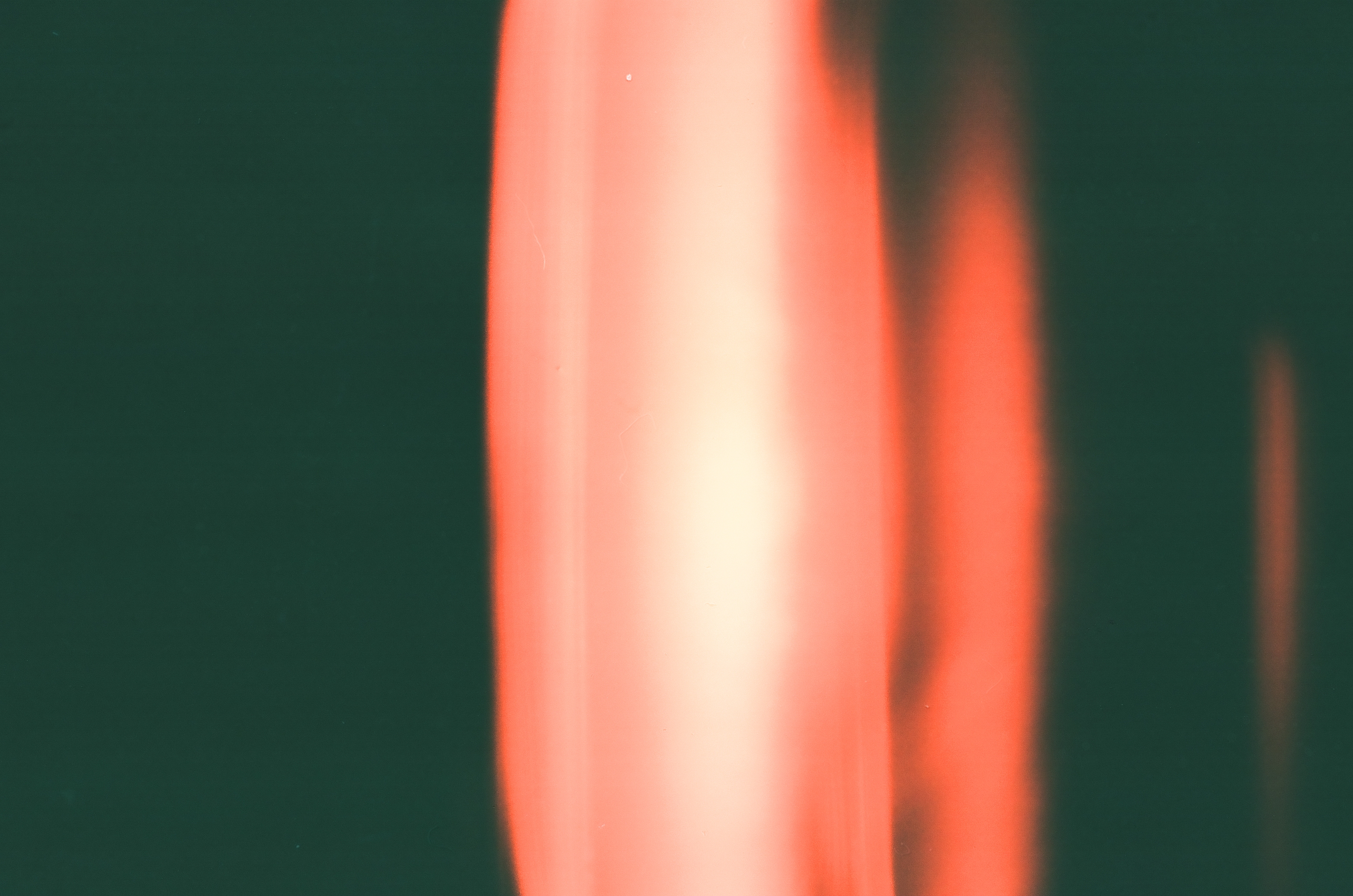 Two vertical bands of blurred pink-white and orange light streak downward against a solid dark green ground, with no other detail visible.