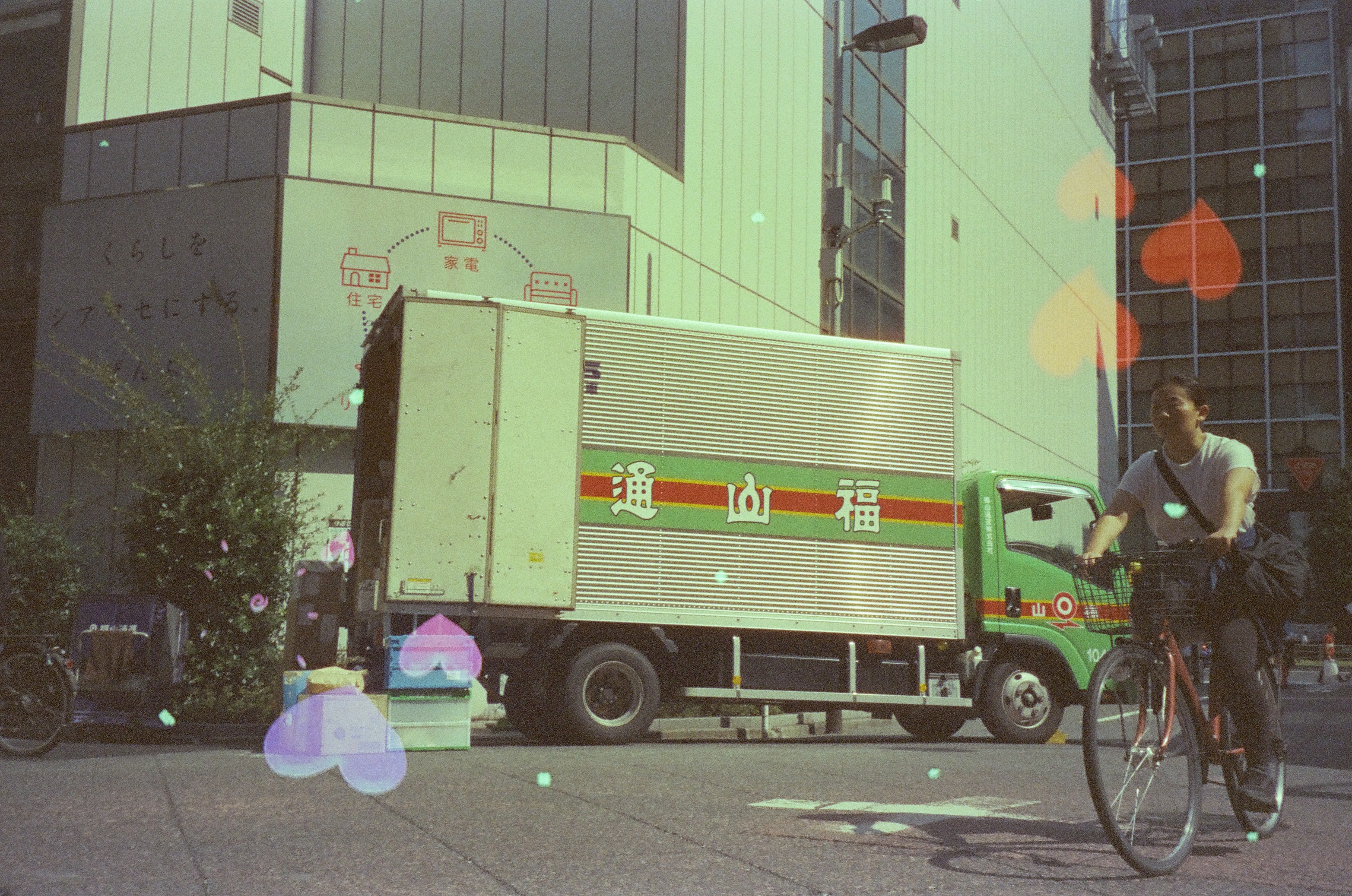 A cyclist passes a green delivery truck while colored heart marks scatter across the street view.