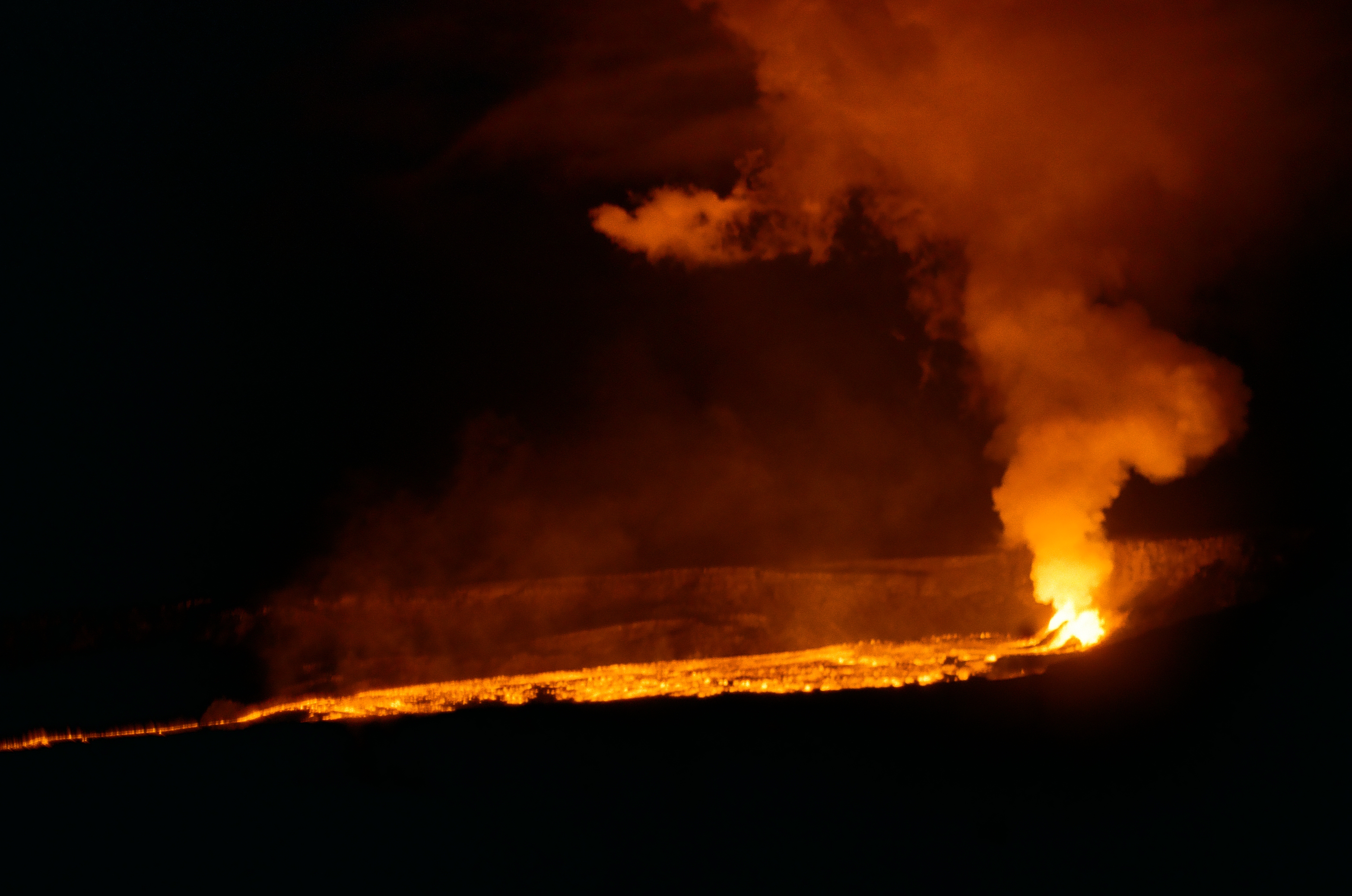 Orange lava glows across black ground while a thick illuminated plume rises from a bright vent.