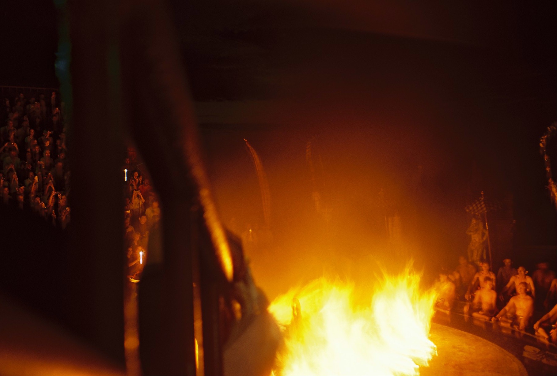A large yellow-orange fire fills the lower center while dark vertical forms obscure people seated around the far edge.